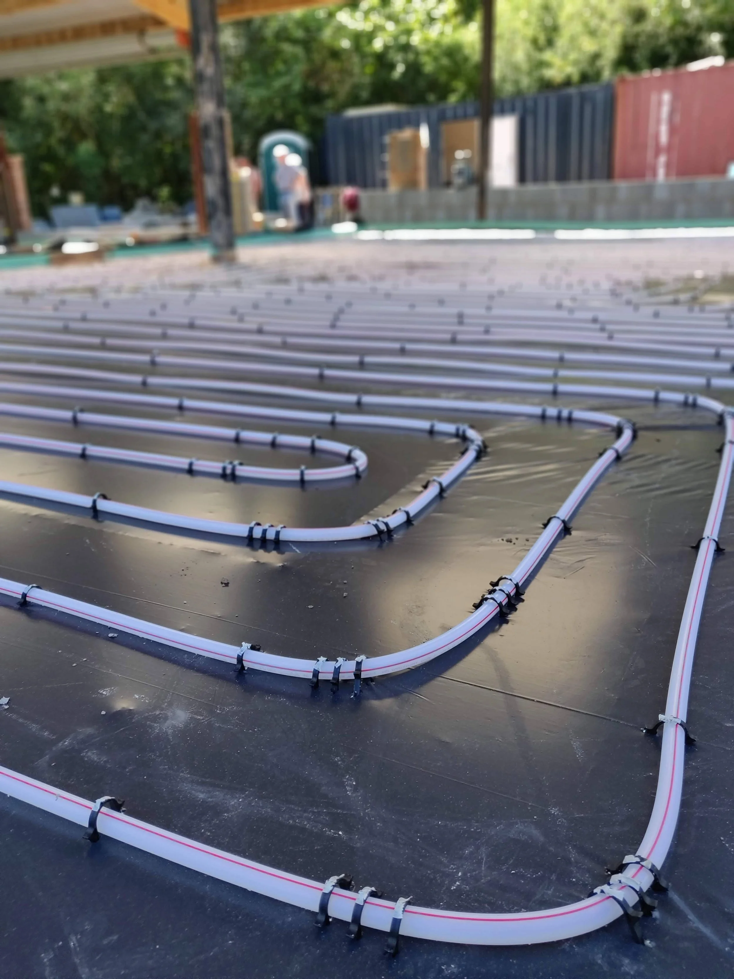 Close-up of white electrical conduits laid out on a flat surface, part of a construction site with unfinished walls, trees, and construction workers visible in the background in Herefordshire