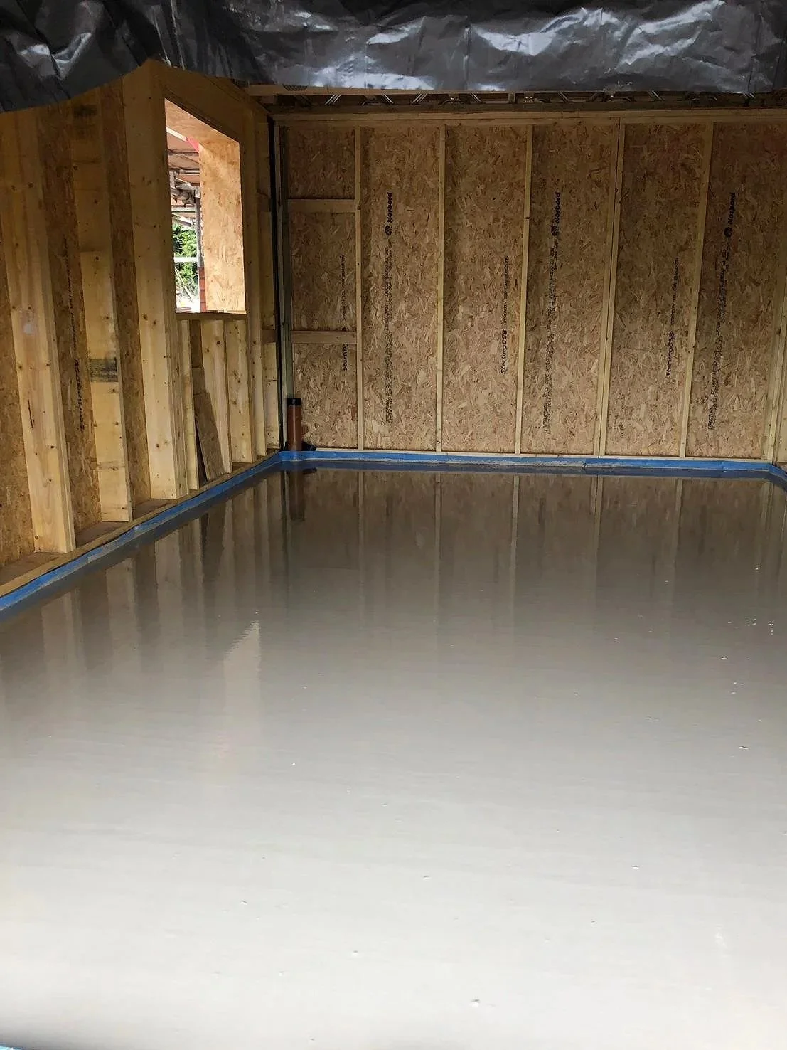 Interior of a building under construction with unfinished wooden framing and a liquid screed floor in West Midlands.