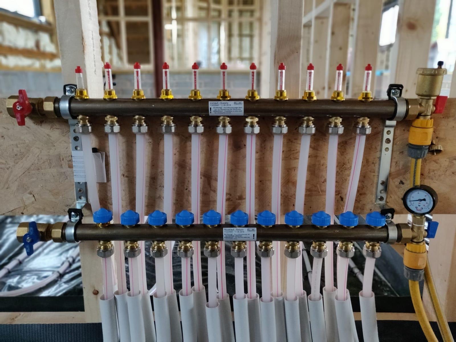 A plumbing underfloor heating manifold system with multiple valves and gauges is installed in a wooden frame, used for controlling water flow in a plumbing setup in Herefordshire.