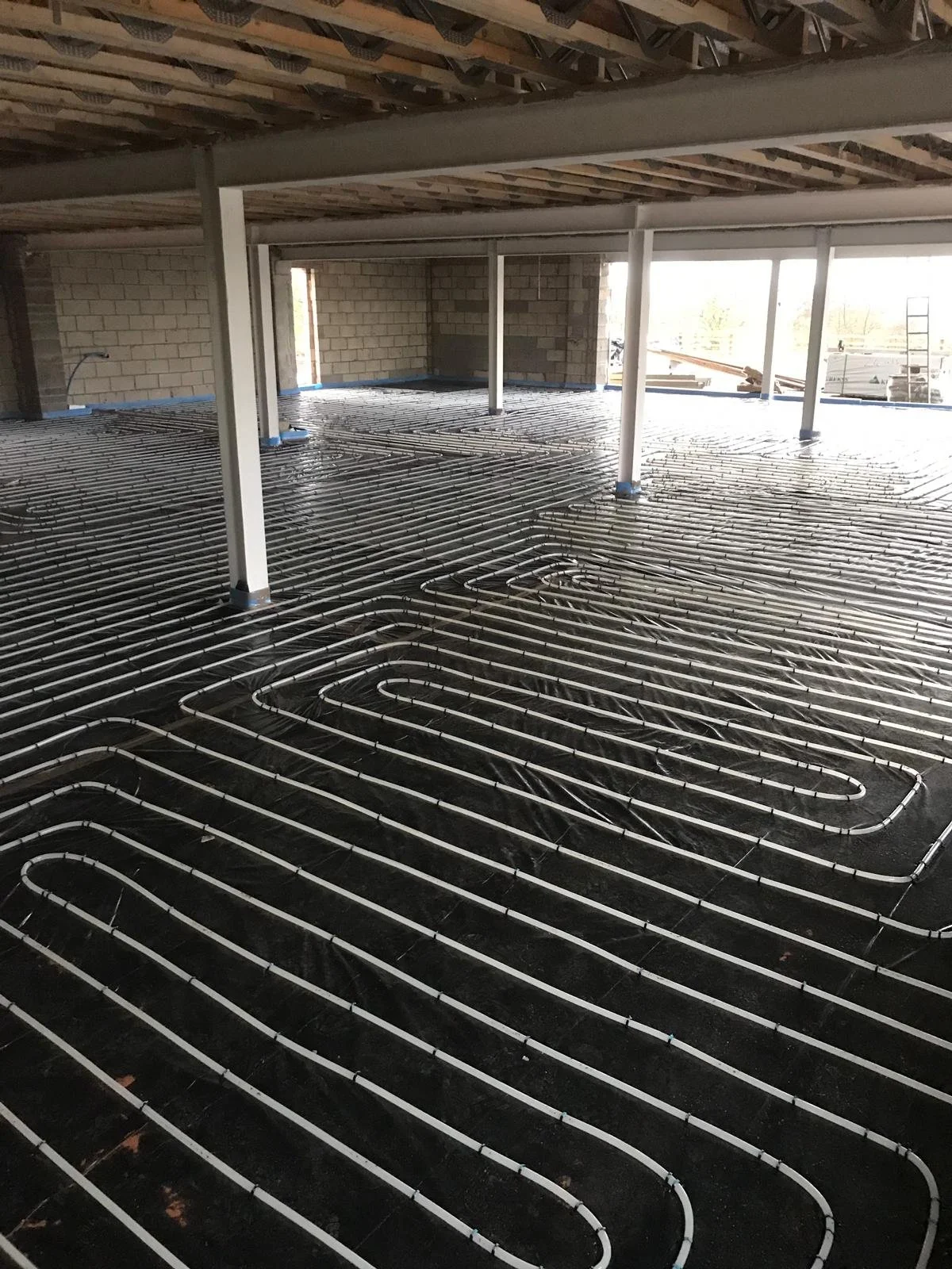 Under construction building with radiant floor heating system installation visible, with pipes laid out on the floor and supported by a black insulation layer in Shropshire.