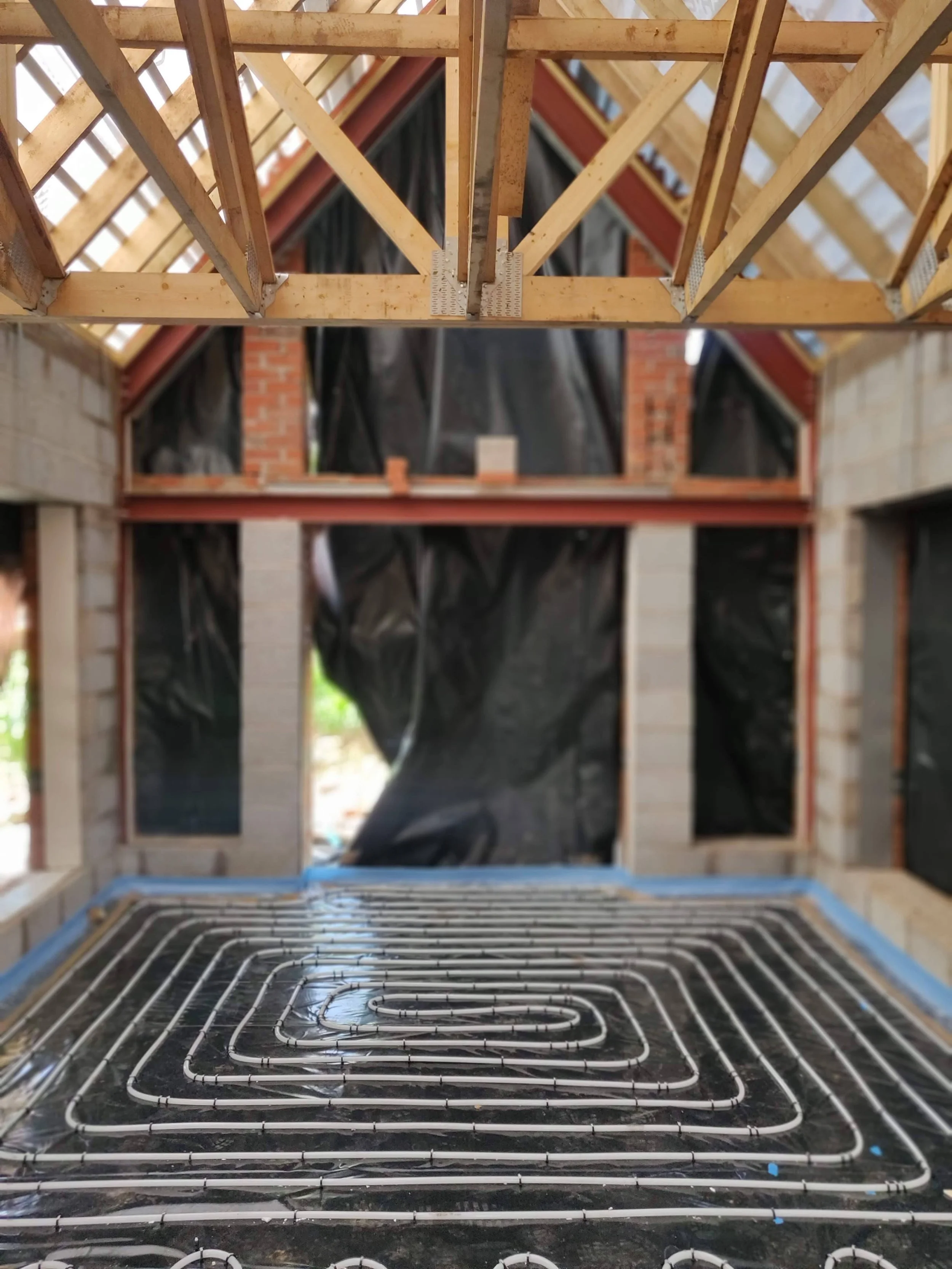 Interior of a house under construction with a view of the roof framing, wall openings, and a radiant floor heating system installed on the floor in Worcestershire