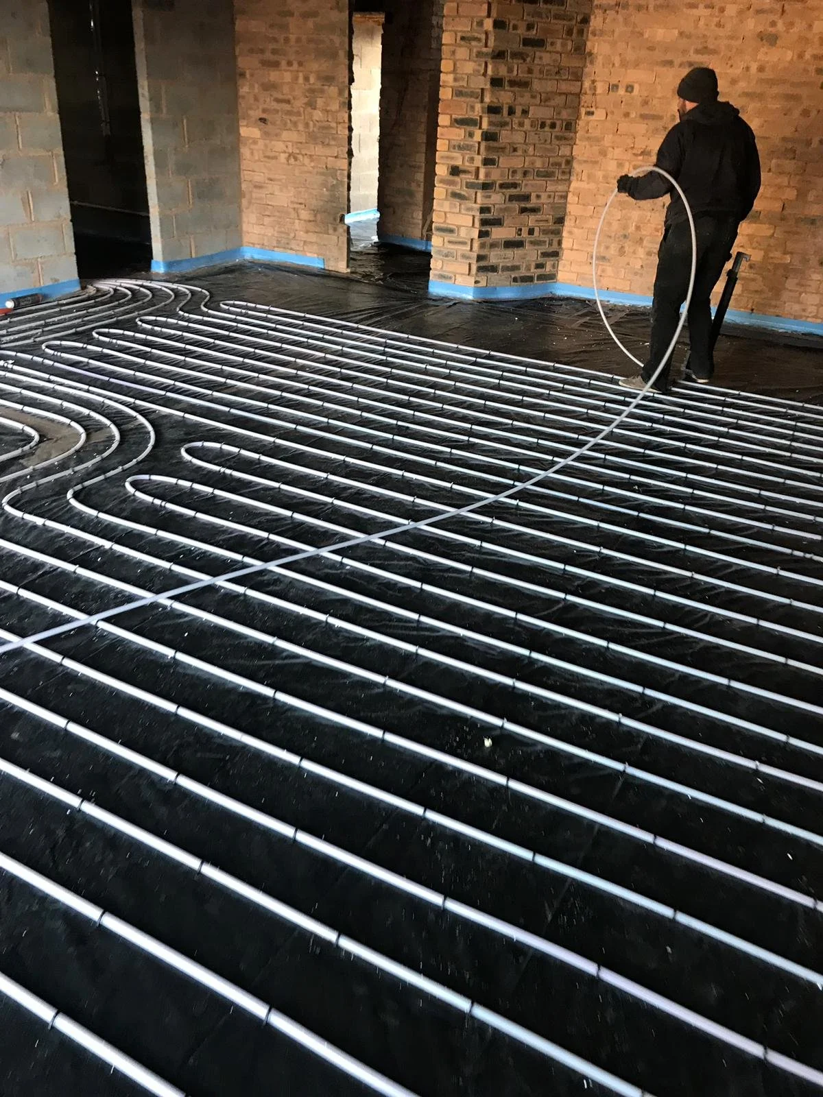 A person installs underfloor heating pipes on a black plastic vapor barrier in a building under construction ready for a liquid screed in Worcestershire