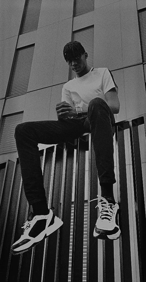 Young man in casual clothes sitting on a railing, looking at his phone, in front of a modern building in black and white.