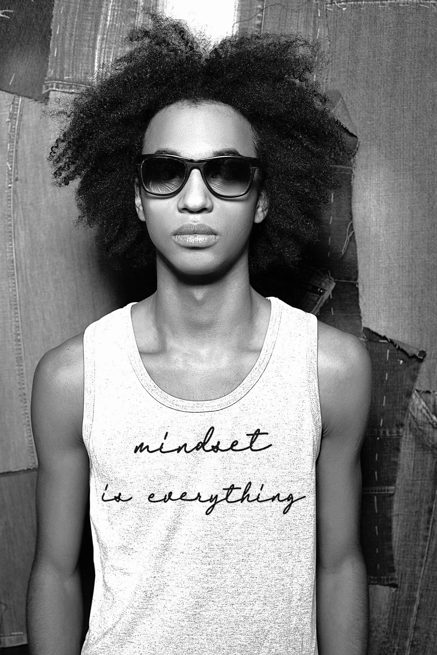 A woman with curly hair wearing sunglasses and a sleeveless shirt that says 'mindset is everything.'