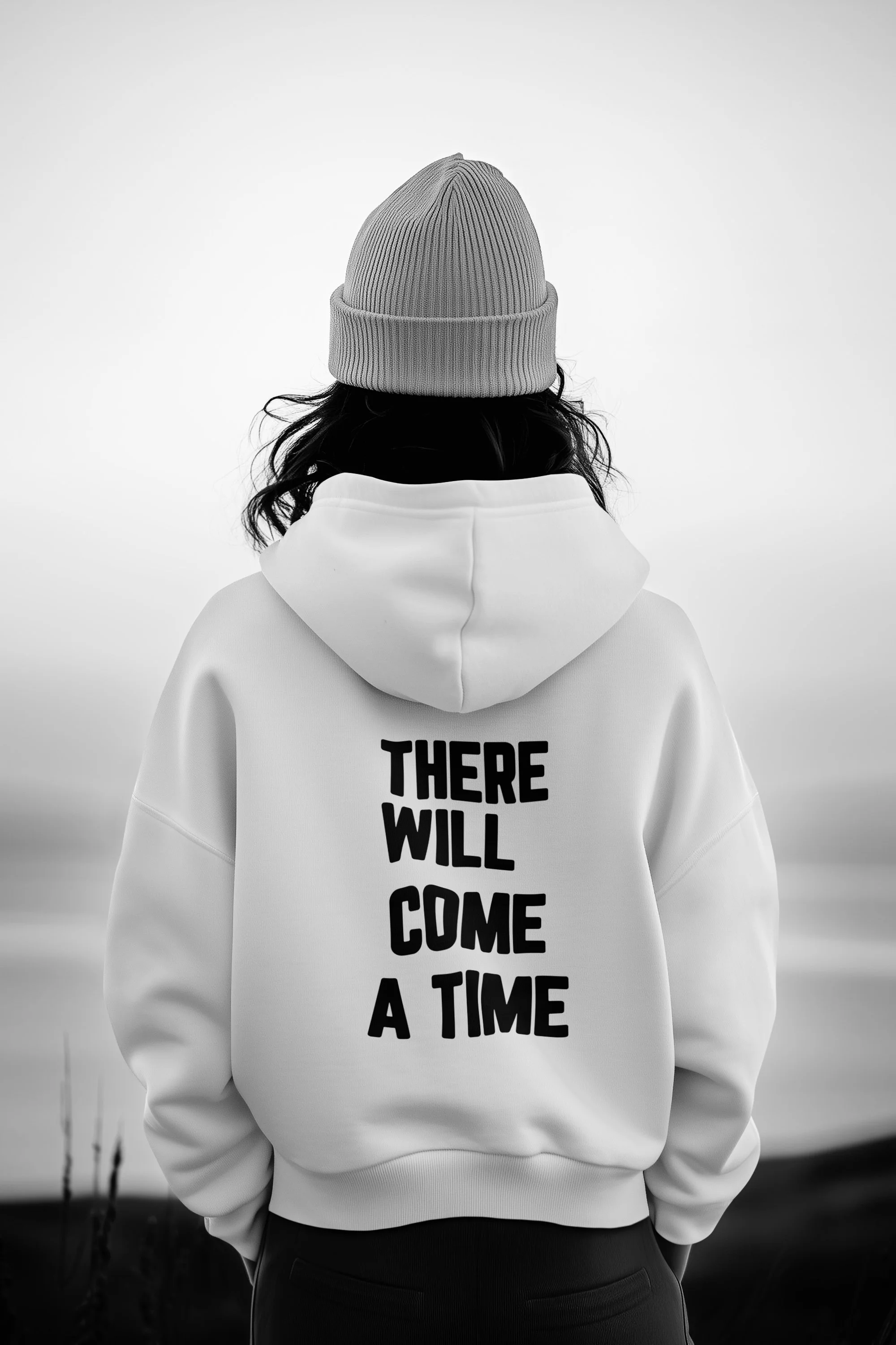 Person wearing a beanie and hoodie with the text "There Will Come A Time" on the back, standing outdoors with blurred background.