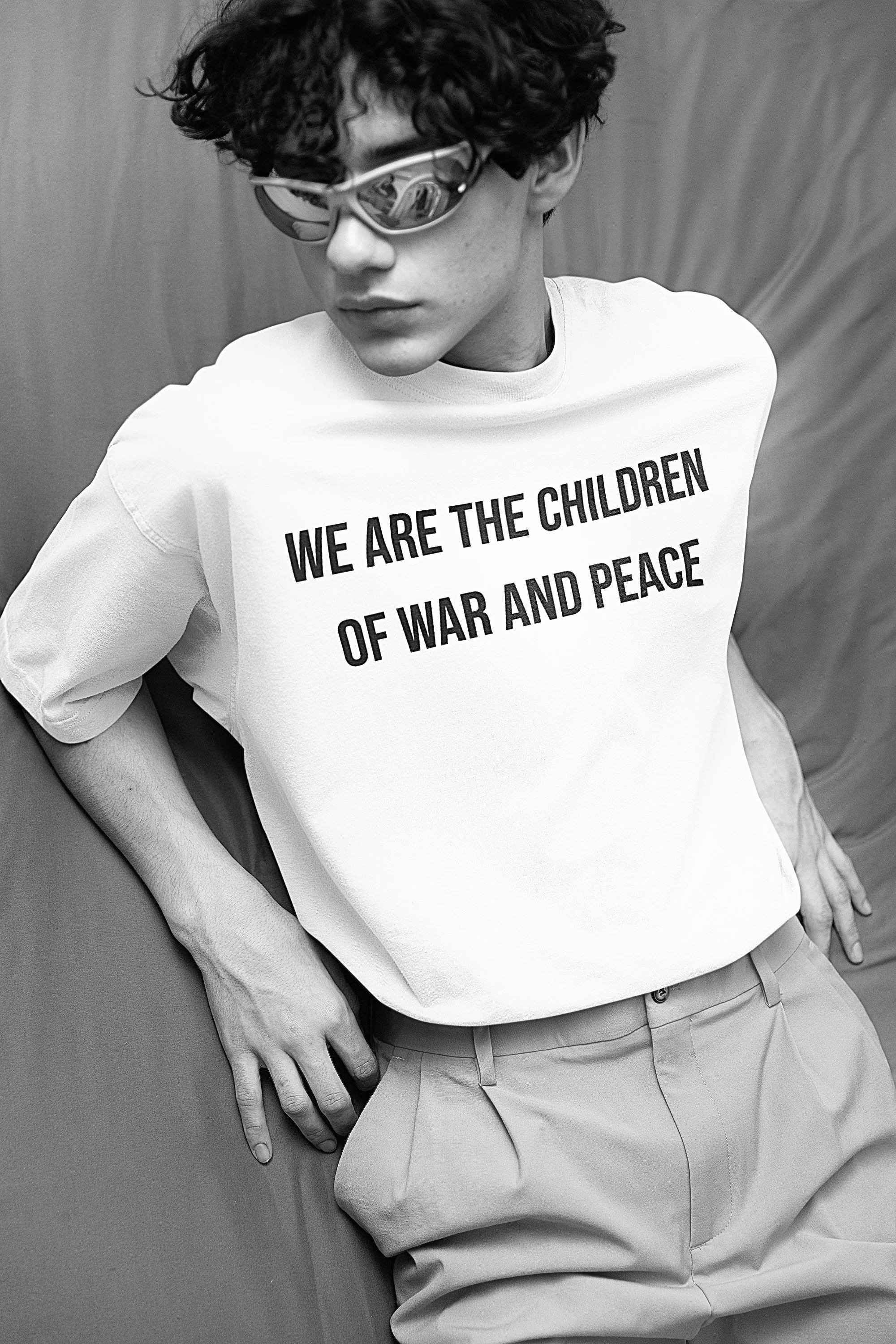 Black and white photo of a young person wearing sunglasses and a T-shirt that reads 'We are the children of war and peace'.