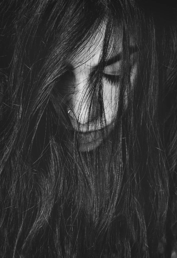 Black and white close-up of a woman with long, messy hair covering part of her face, with her eyes closed.