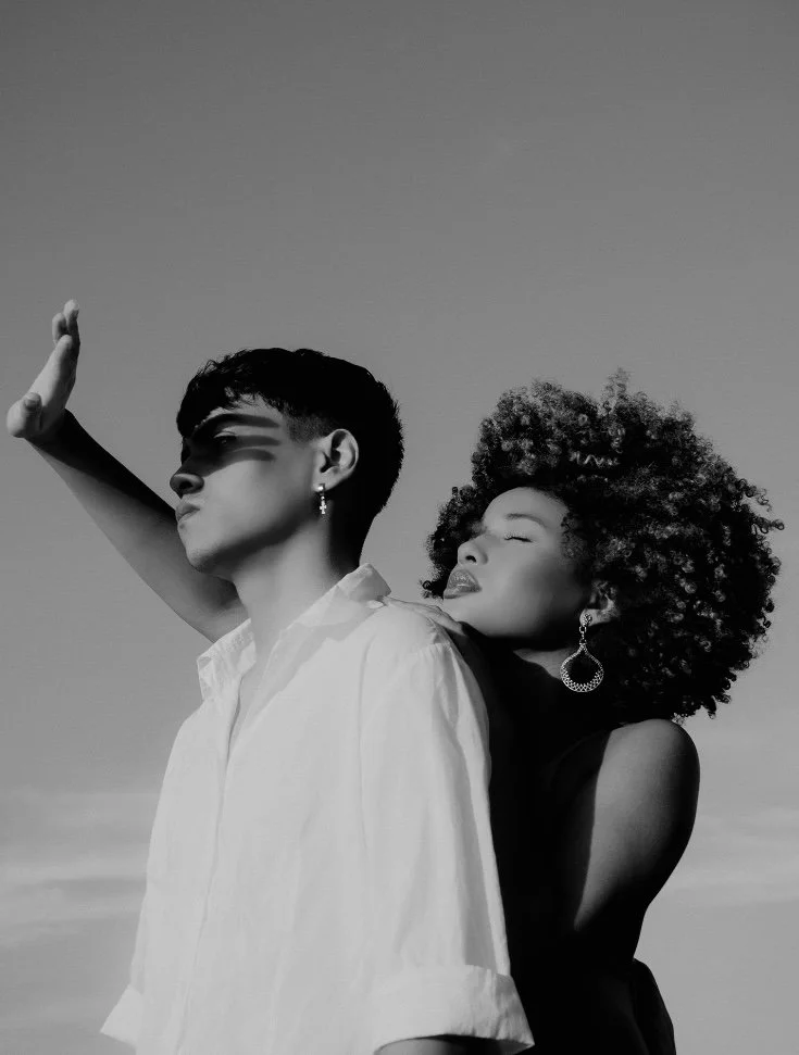 A black and white photo of two women outdoors, one with short hair and the other with curly hair, embracing each other.