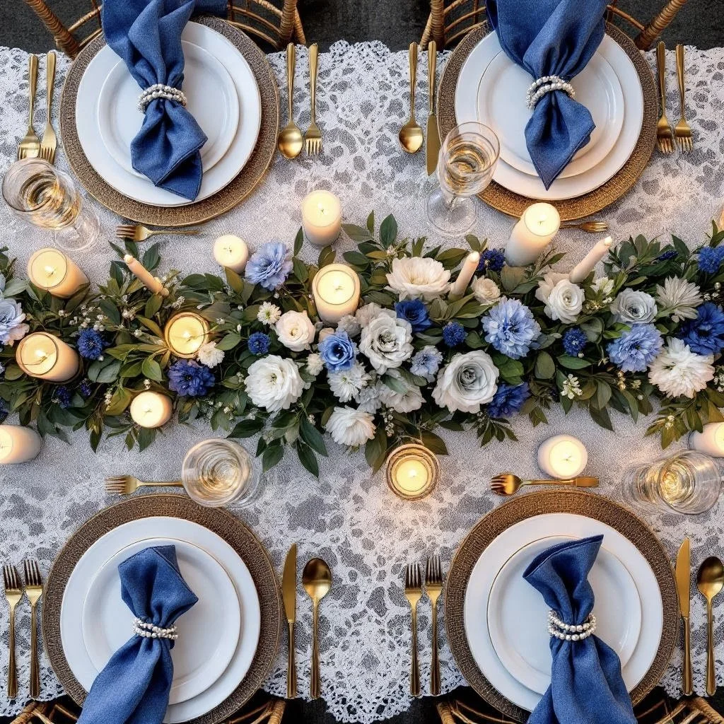 Table setting with gold-rimmed white plates, blue cloth napkins tied with pearl rings, gold flatware, glasses of water, and an arrangement of white and blue flowers with candles on a lace tablecloth.