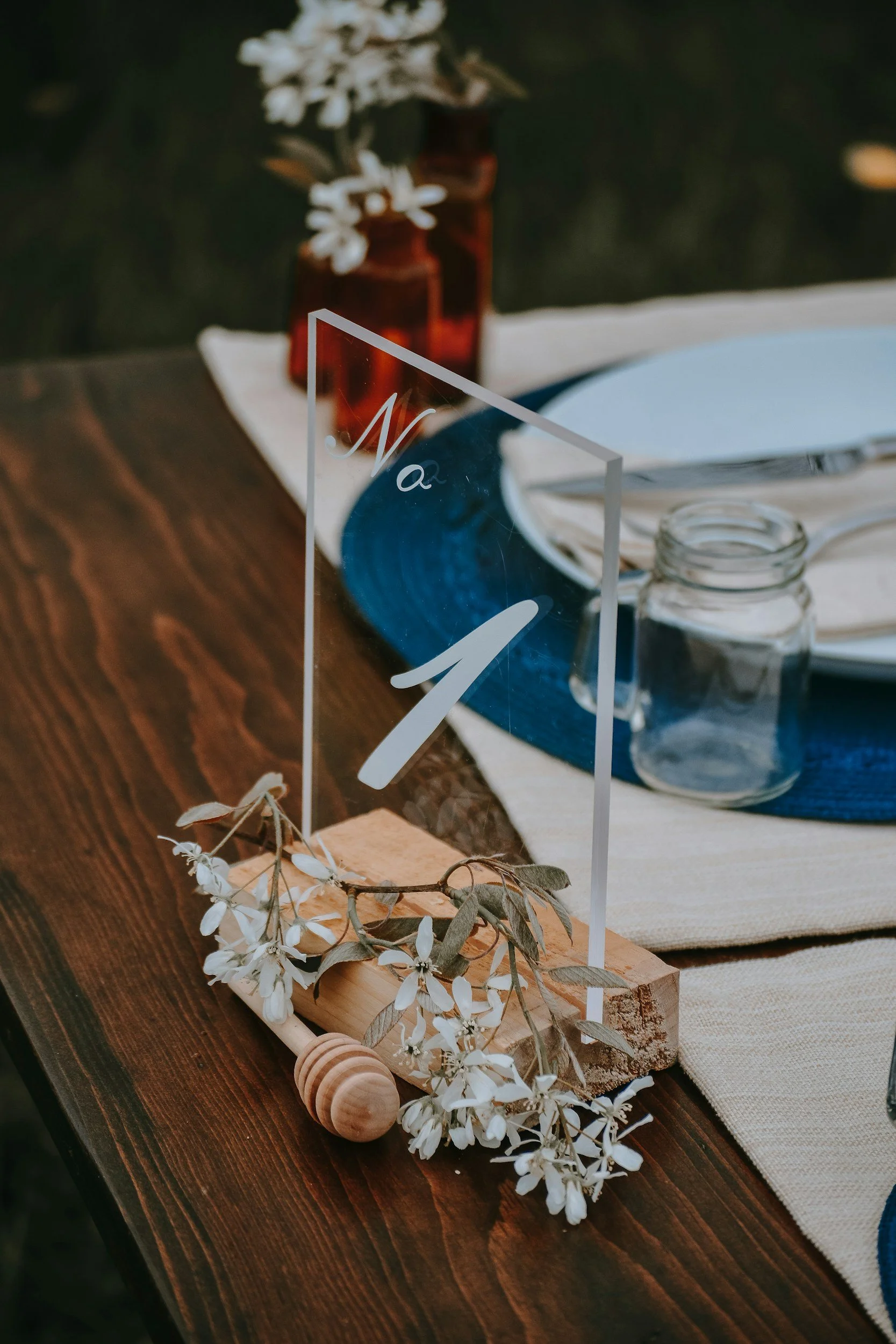 Table setting with a table number sign, white flowers, a mason jar, and plates with utensils.