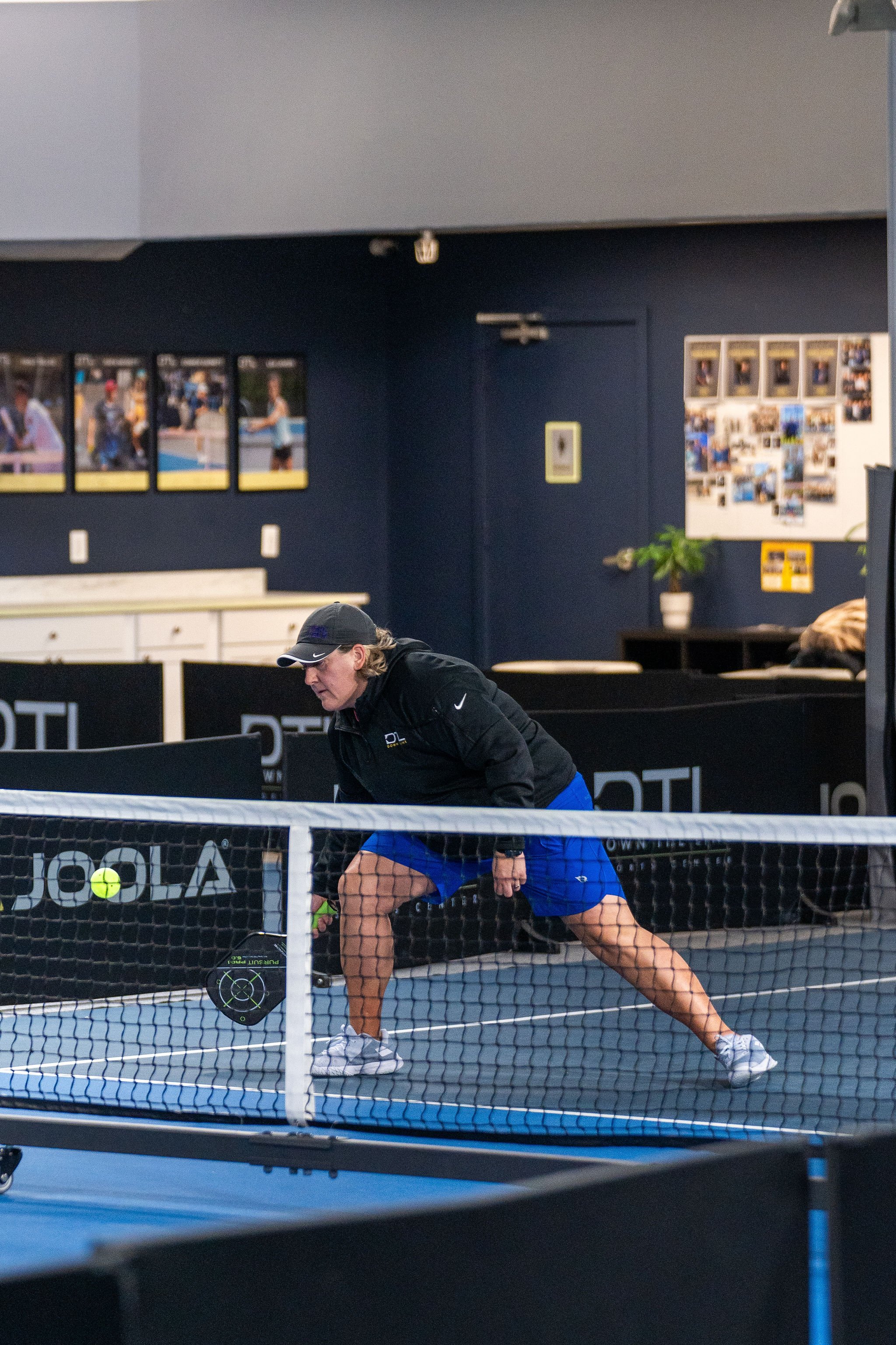 A woman playing pickleball on an indoor court, preparing to hit the ball with her paddle.