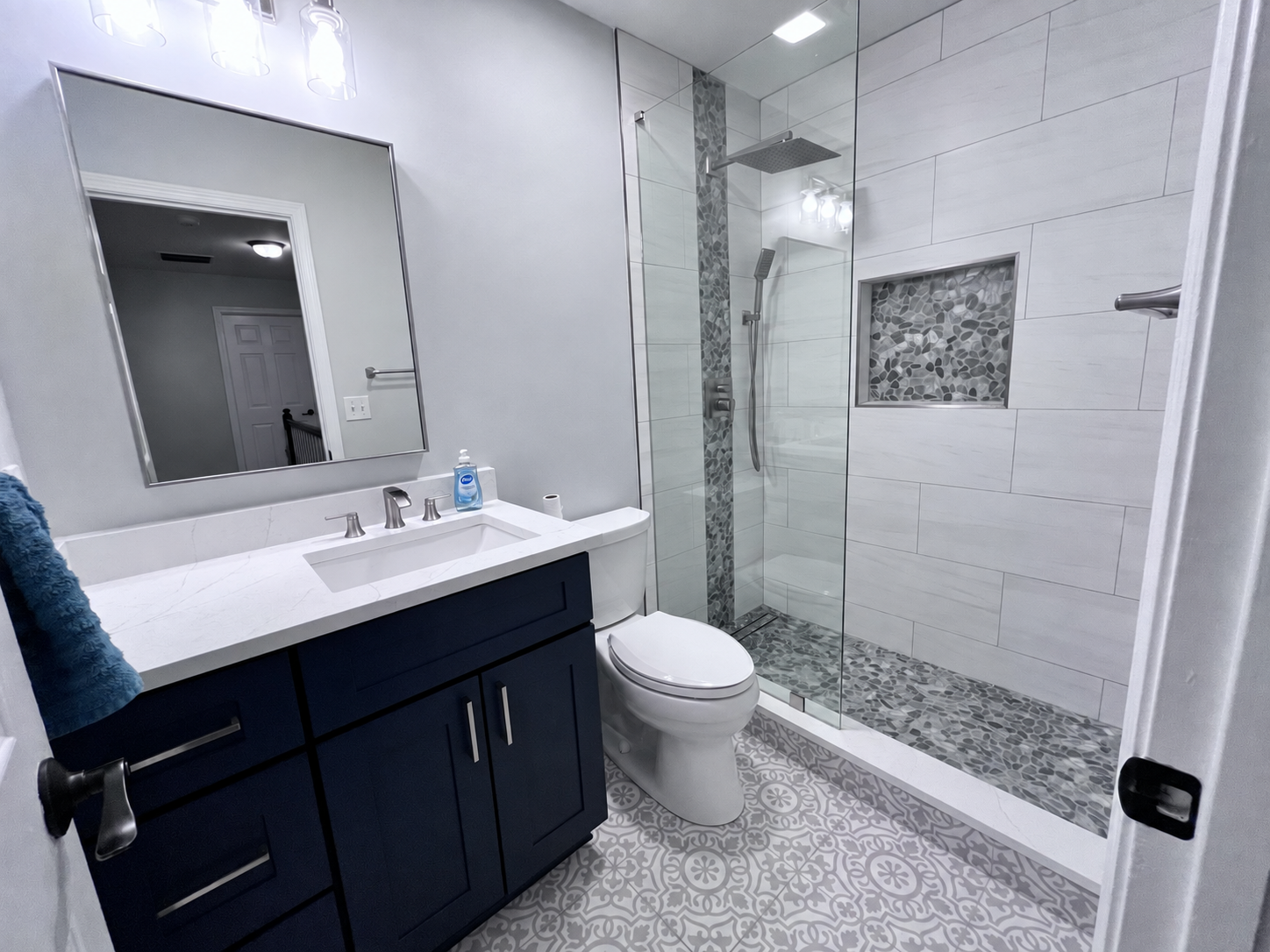 Navy bathroom vanity with glass shower and patterned floor