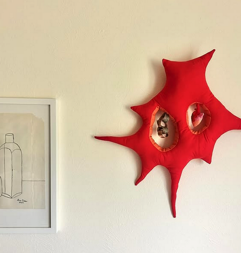 Red star-shaped wall art with hollow centers on a beige wall, next to a framed sketch of a bottle.
