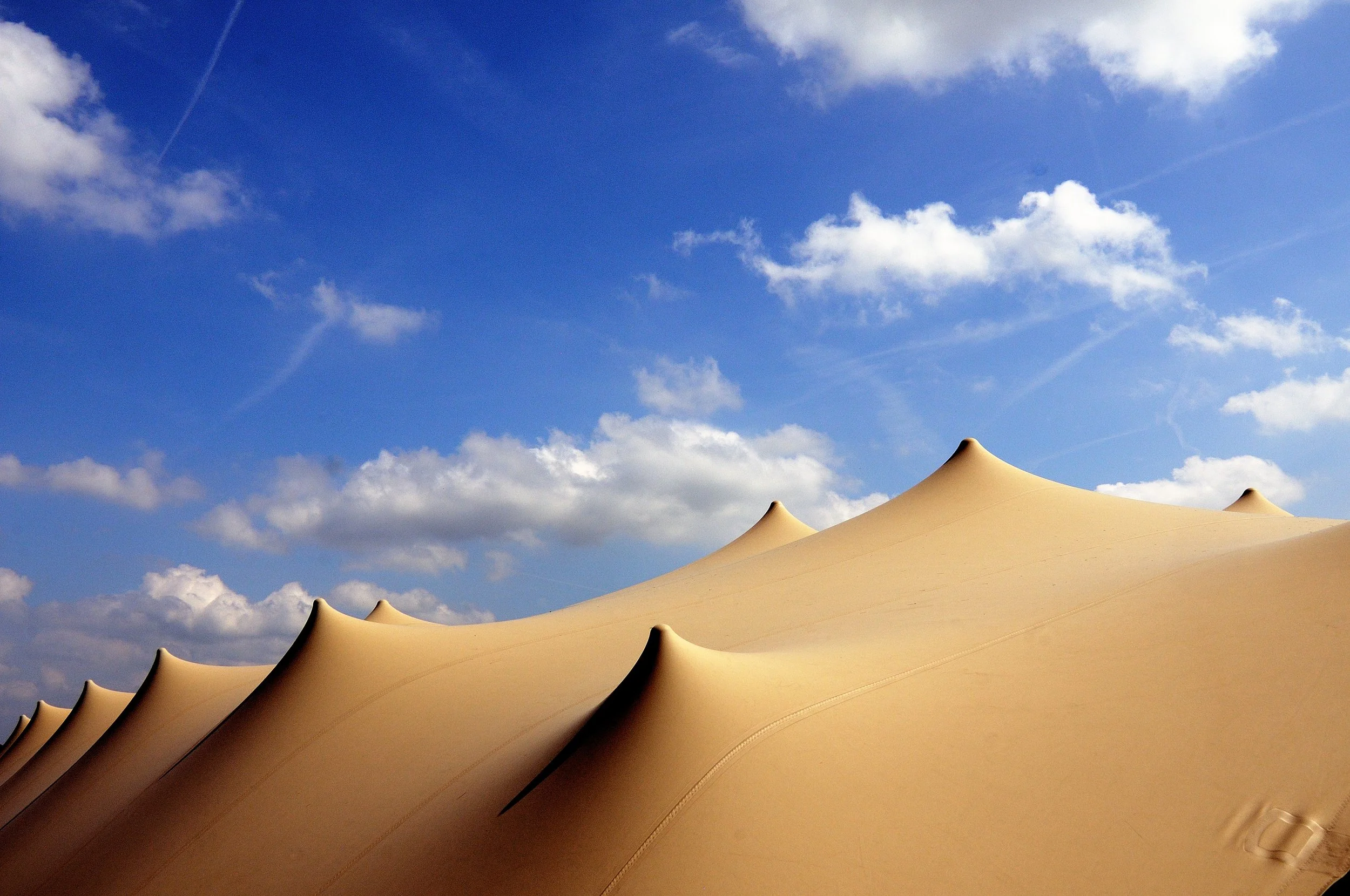Close-up of a beige beach tent with pointed peaks against a blue sky with scattered clouds.