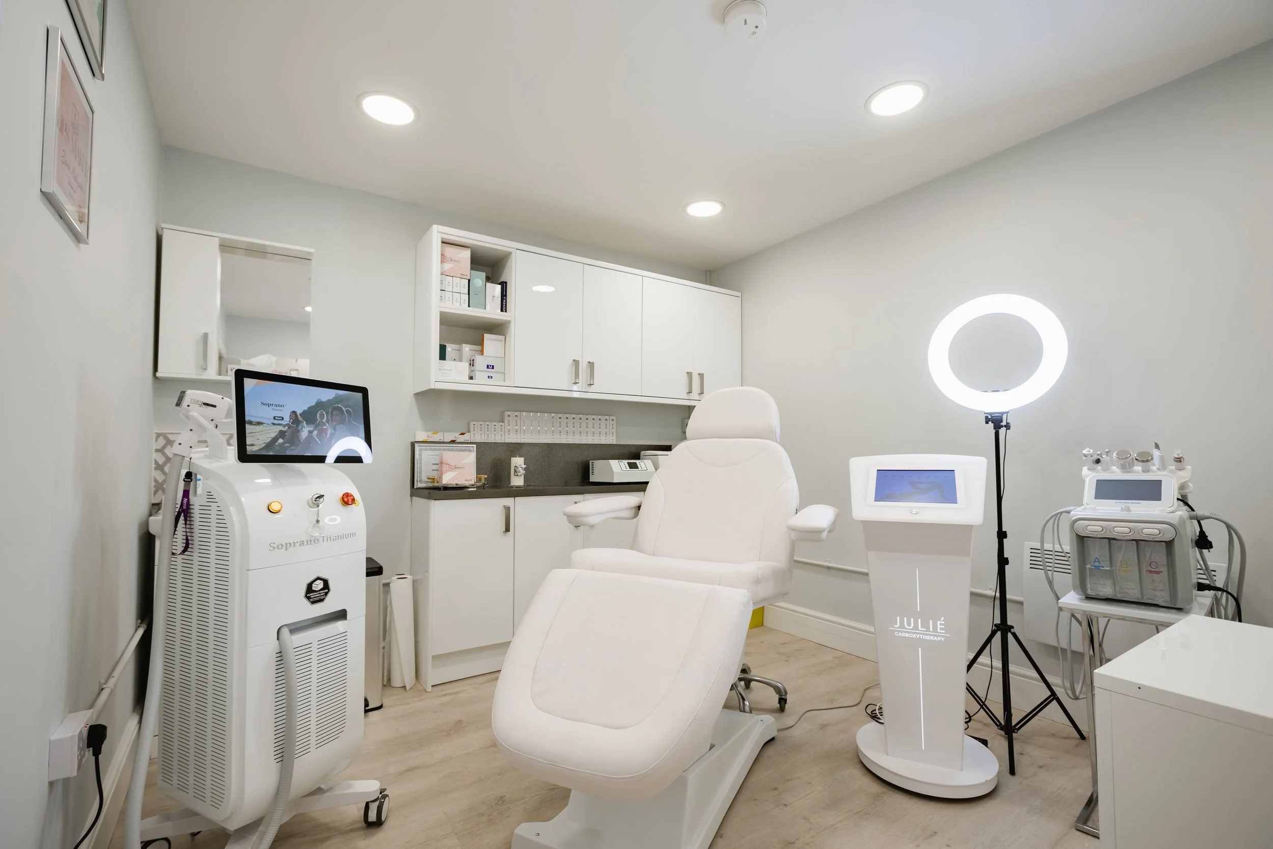Medical spa room with a white treatment chair, medical equipment, a ring light, and cabinets