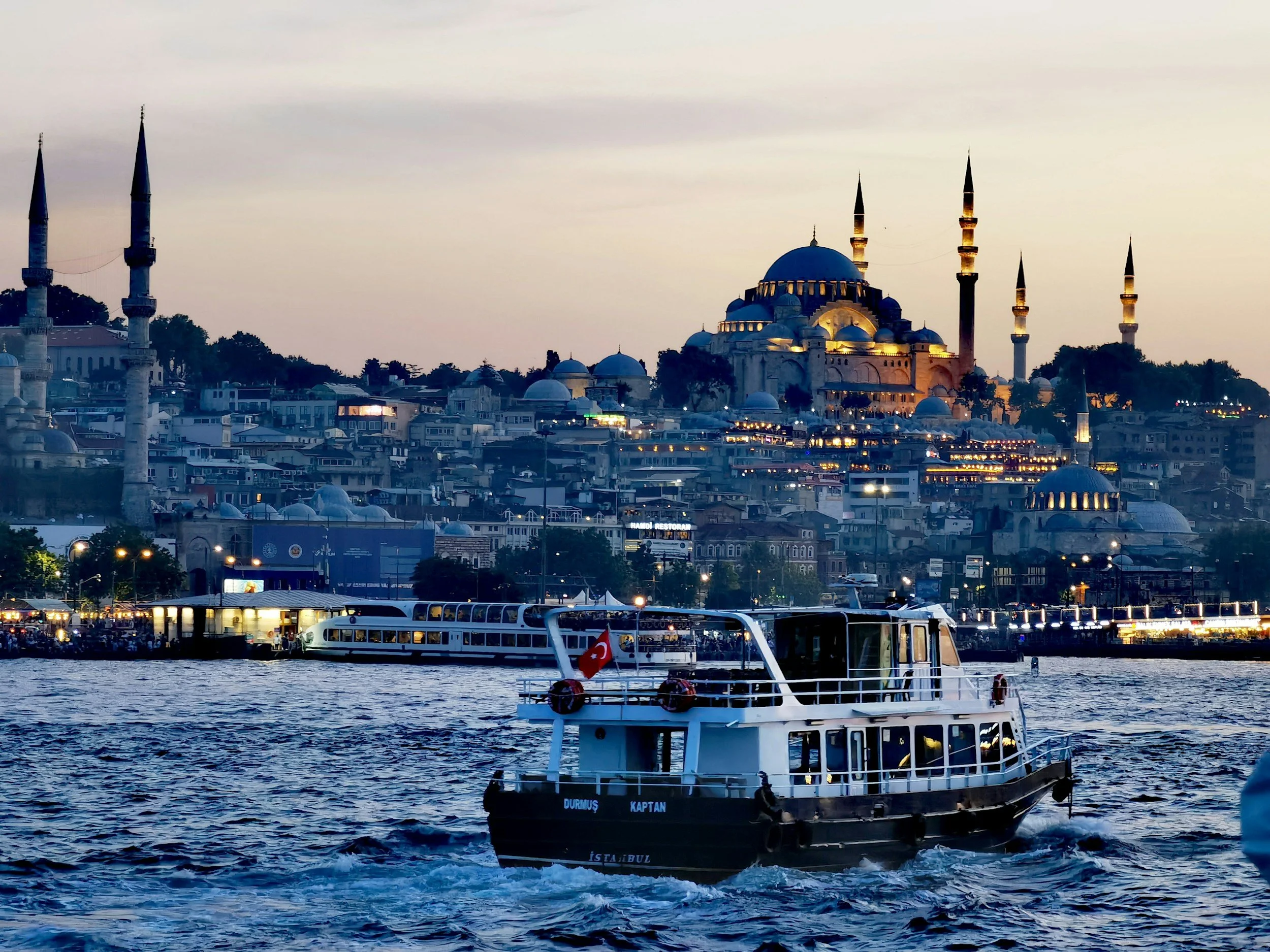 A boat on the Bosphorus Strait with the Suleymaniye Mosque illuminated in the background during dusk in Istanbul, Turkey.
