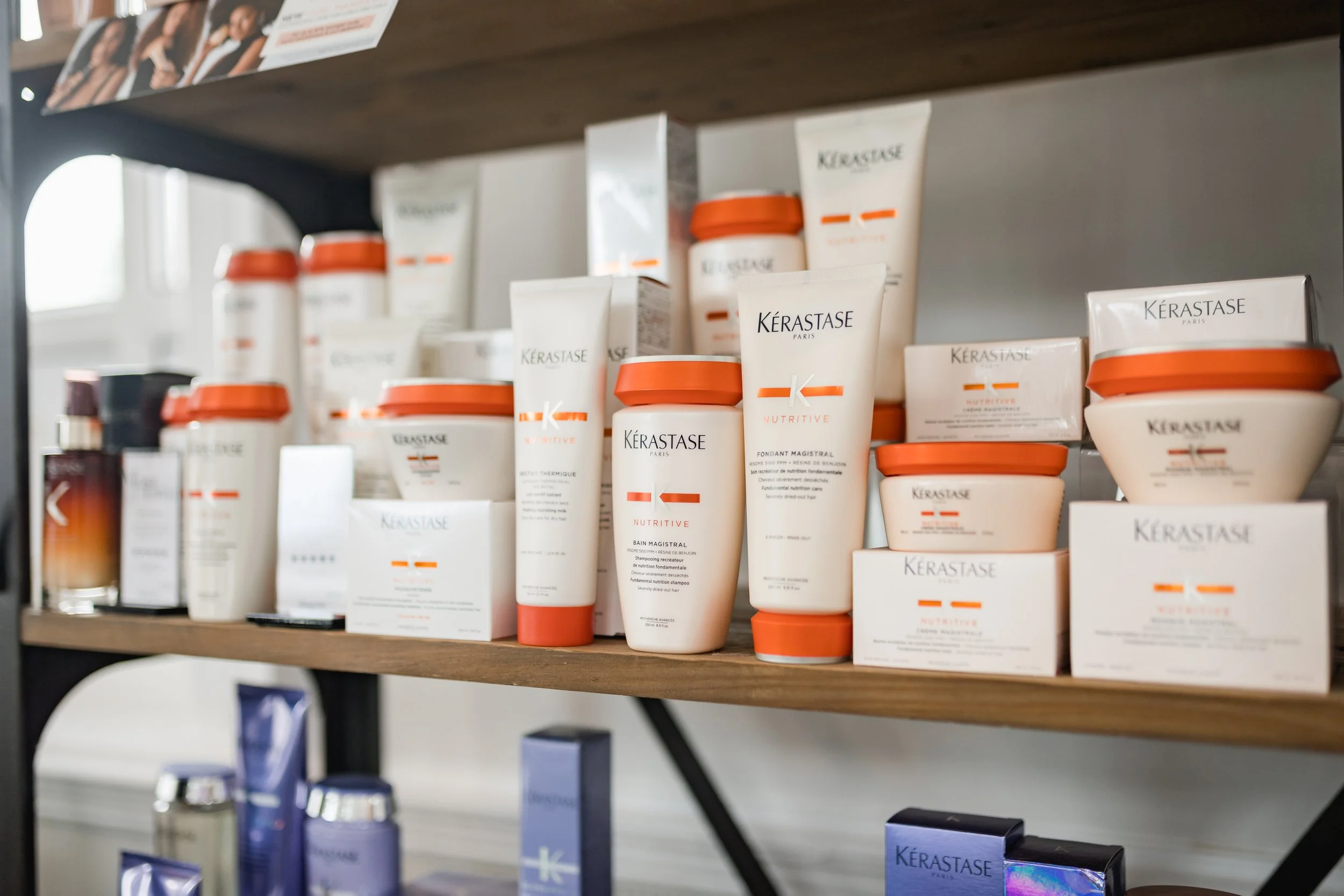 Shelf displaying several bottles and containers of Kérastase hair care products, mainly in white bottles with orange caps.