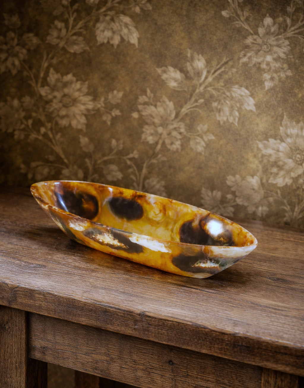 Eine bunte, marmorierte Schale aus Stein auf einem Holztablett vor einem Wand mit floralem Muster.