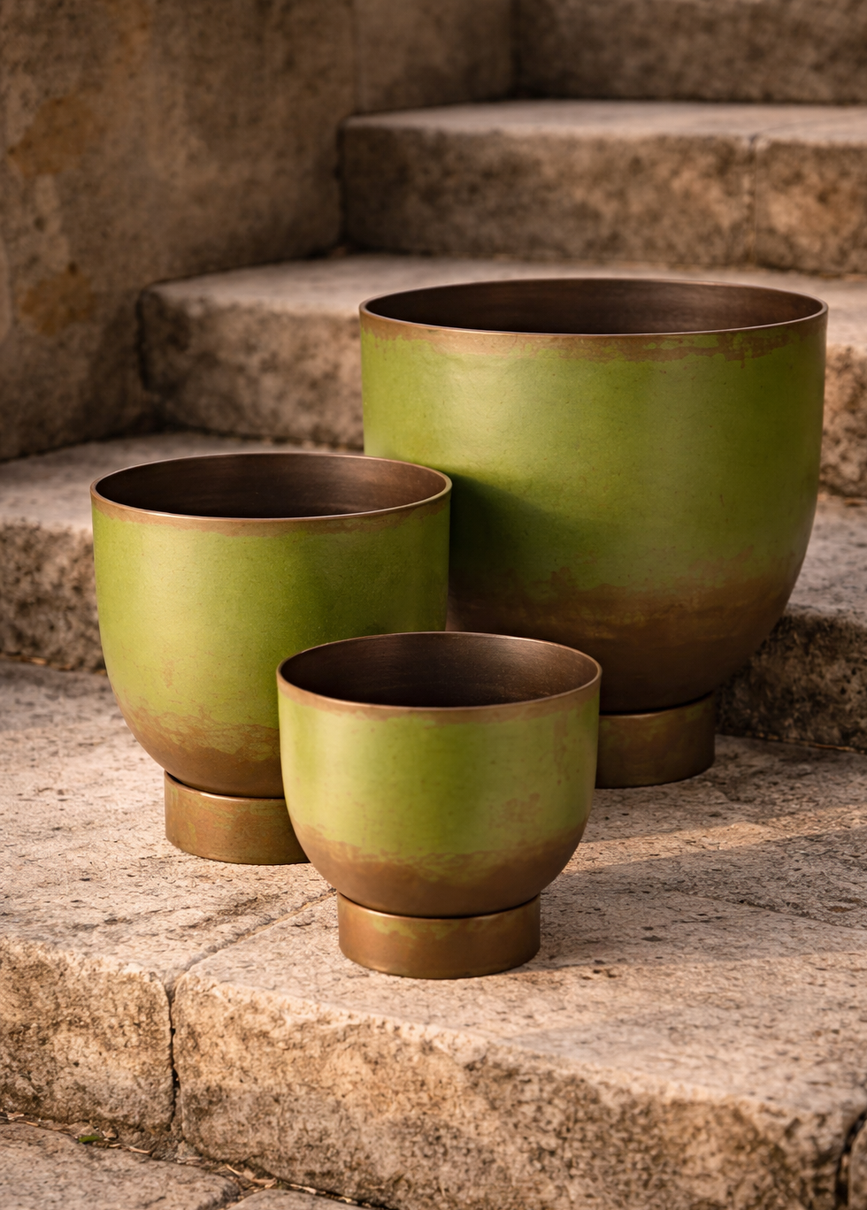 Drei grüne Blumenschalen aus Metall stehen auf einer Steintreppe.