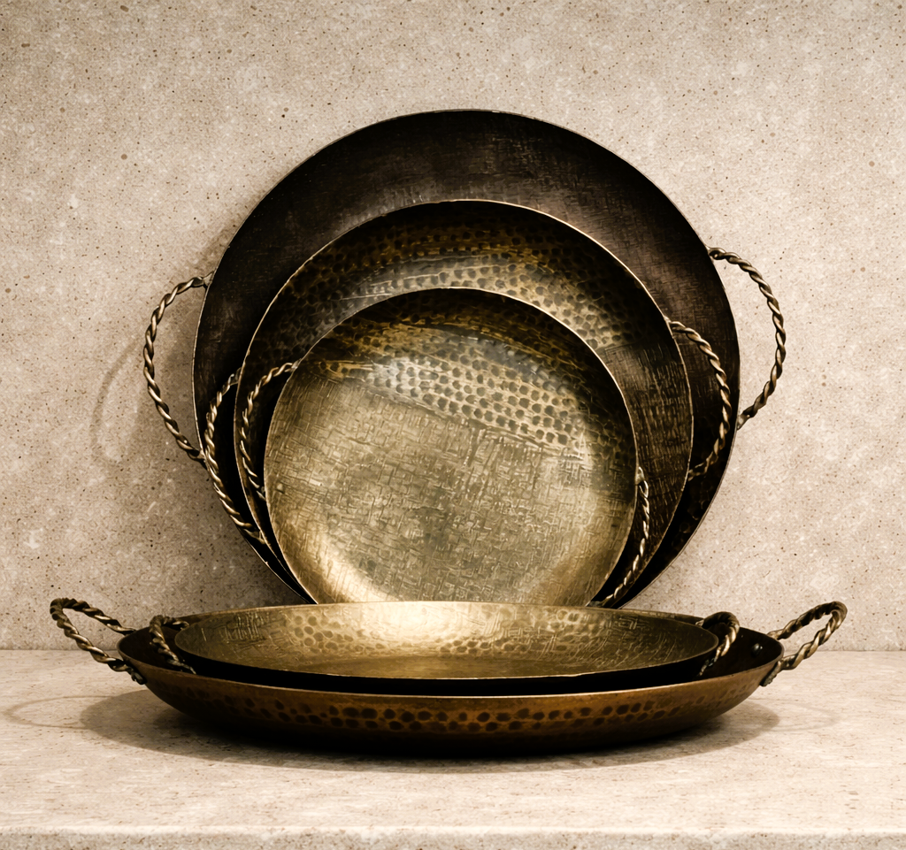 Vier verschieden große goldene Schalen mit Metallgriffen, gestapelt vor einer neutralen Wand