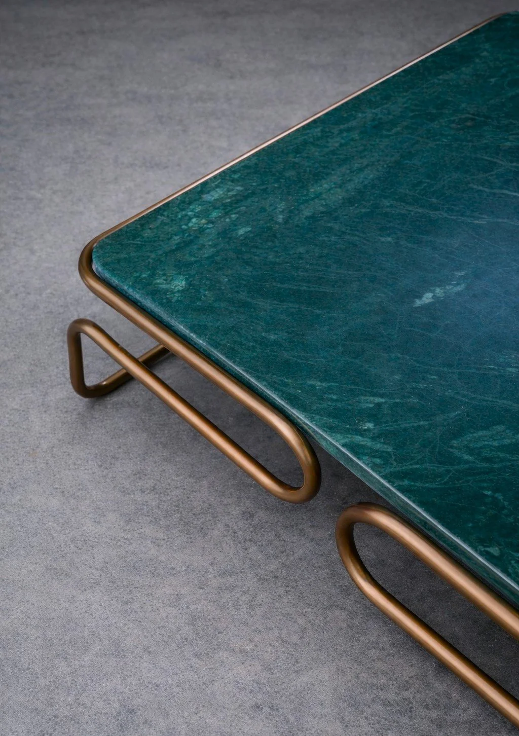 Ansicht auf eine Marmor-Tischplatte in Türkis mit goldfarbenem Metallgestell auf grauem Boden.