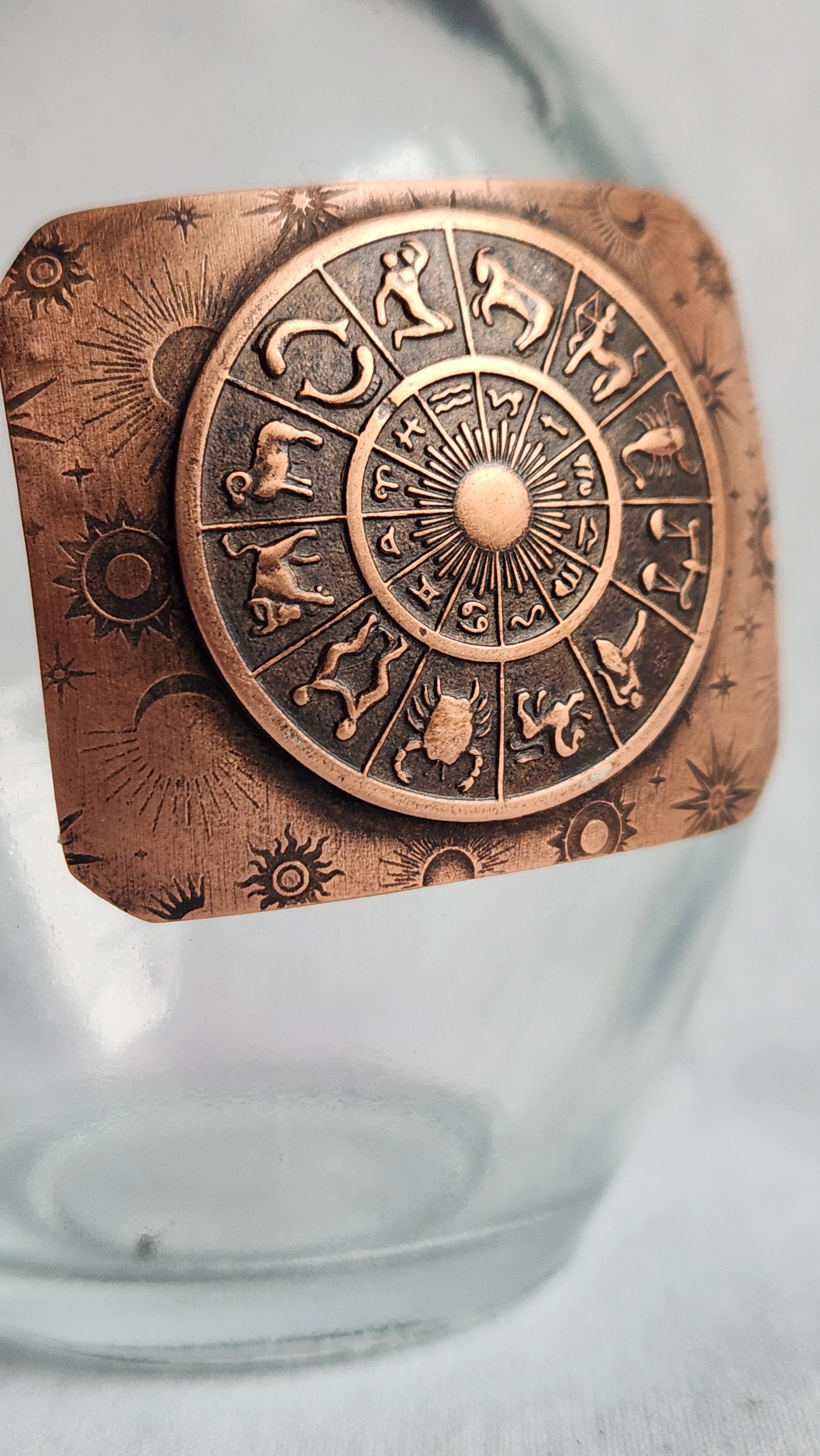 Detail of a die-struck copper zodiac wheel on a glass propagation vase.