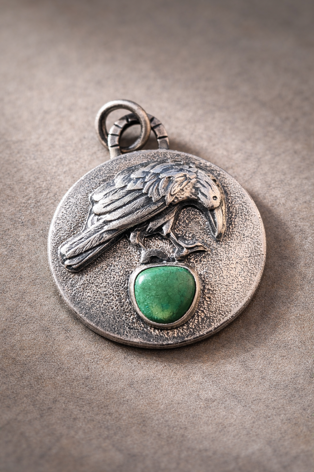 Die-struck and hand fabricated round sterling silver necklace with raven and green turquoise stone.