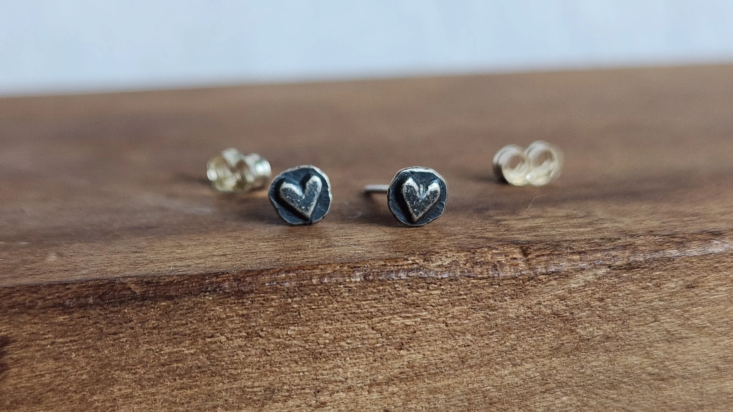 Die-struck sterling silver stud earrings featuring a tiny oxidized heart.