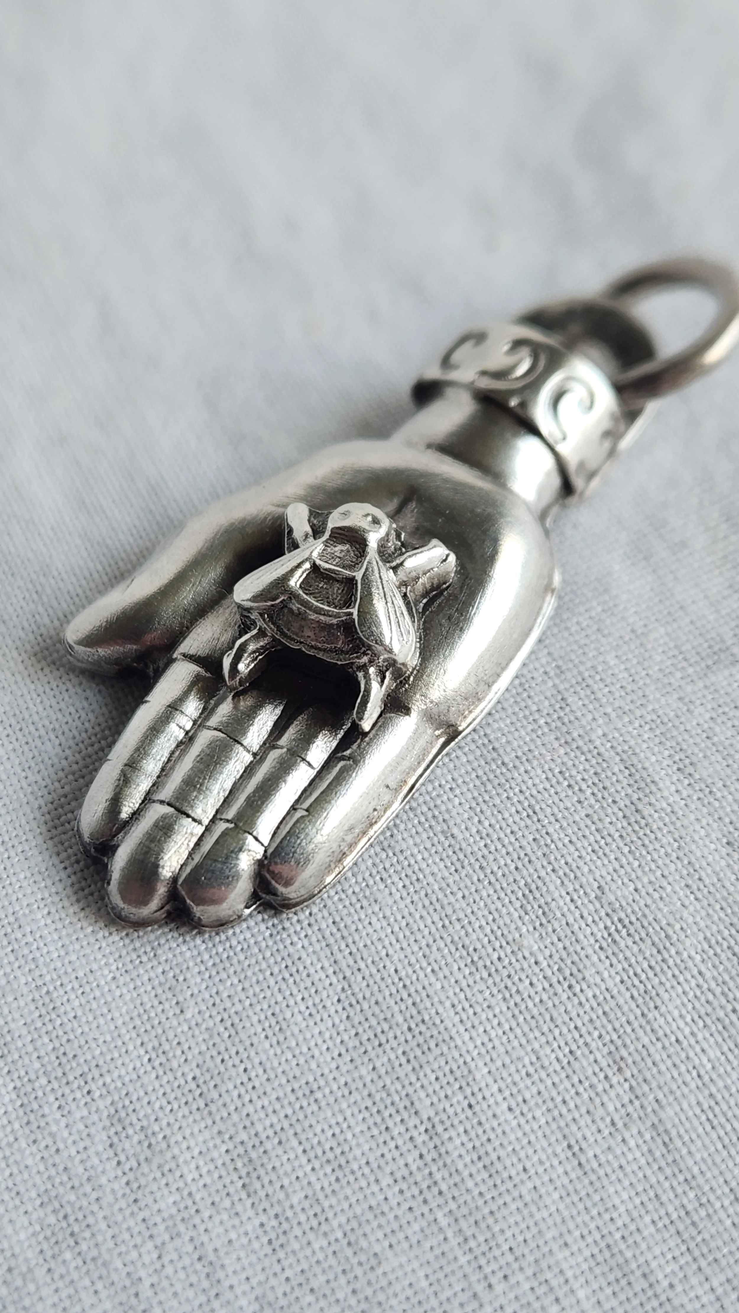 Die-struck and hand fabricated sterling silver pendant necklace with a bee on an outstretched hand.