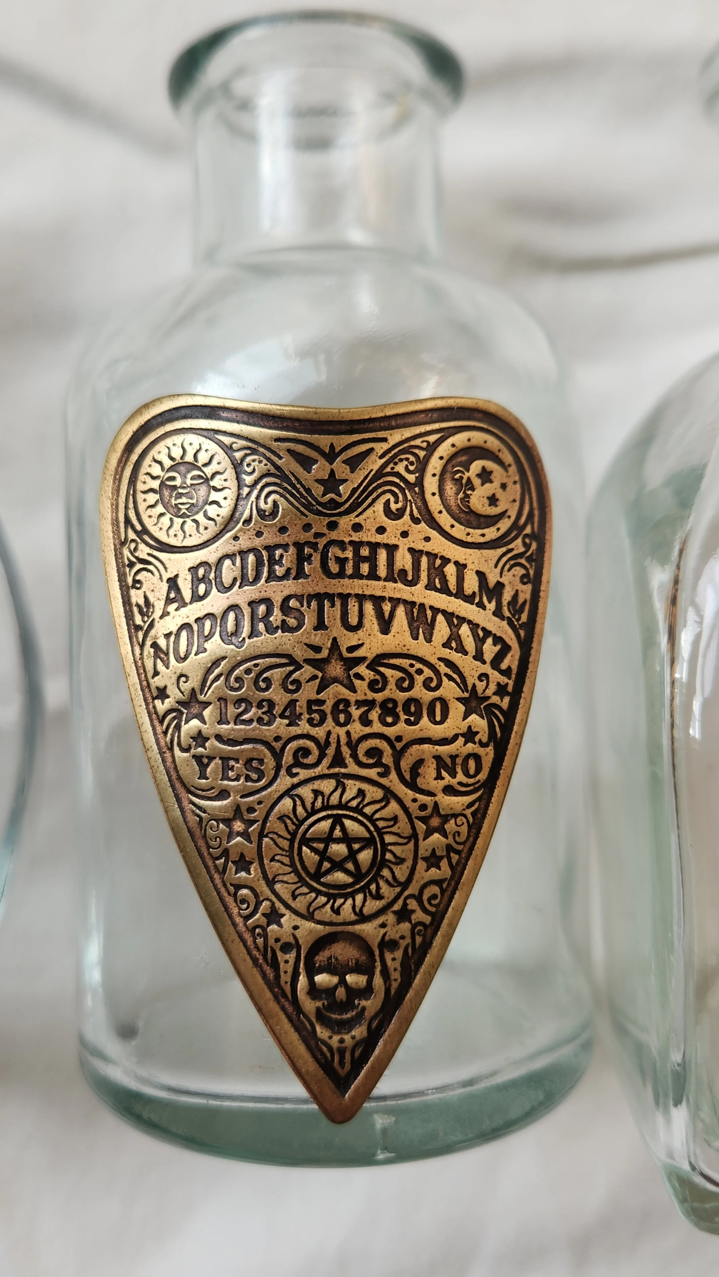 Glass propagation vase embellished with a brass roll printed decorative ouija planchette.