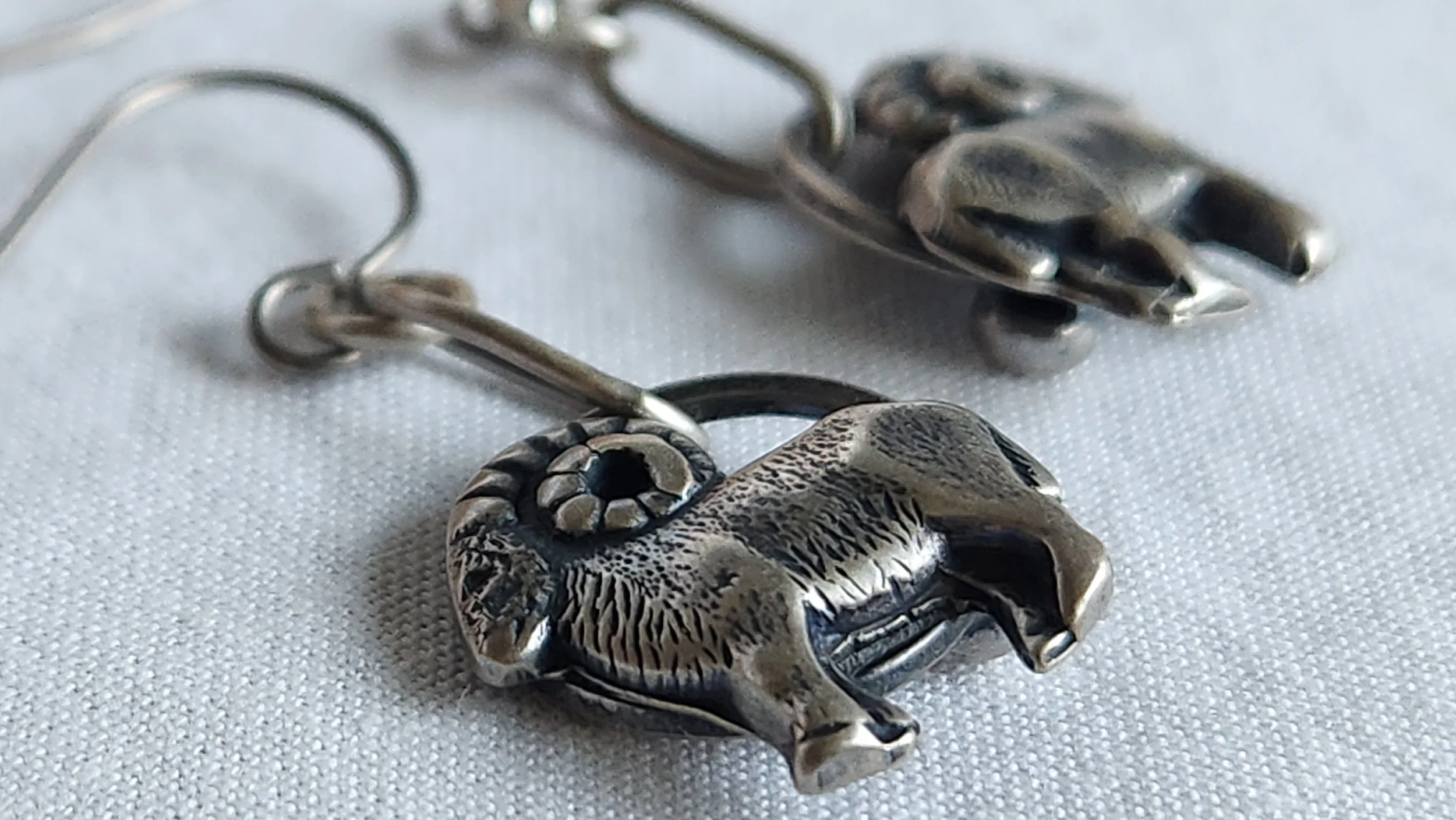 Die-struck and hand fabricated sterling silver drop earrings with rams faced in opposite directions.