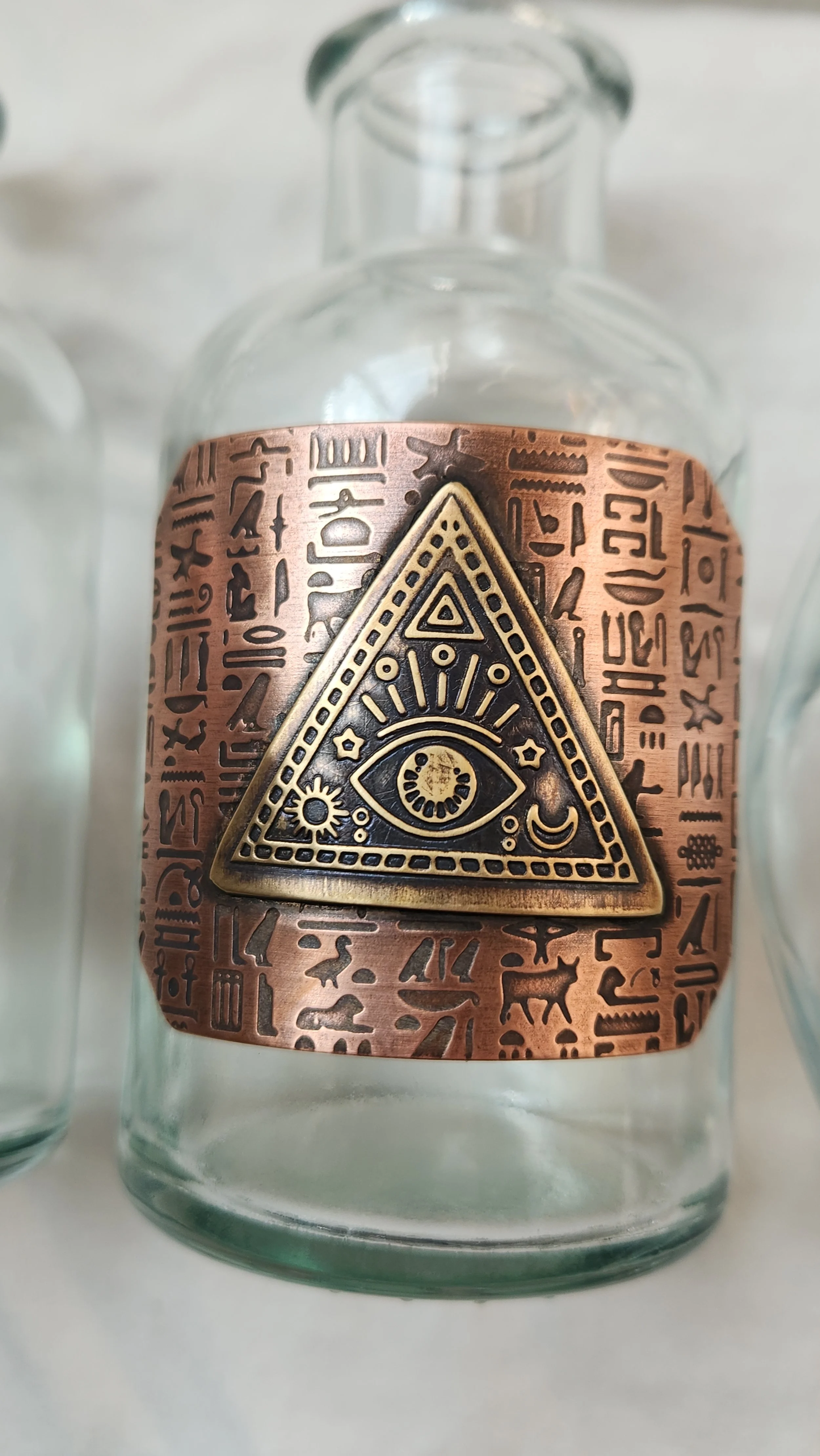 A glass propagation vase featuring roll-printed copper with Egyptian hieroglyphics and a die-struck brass pyramid with eye inside.
