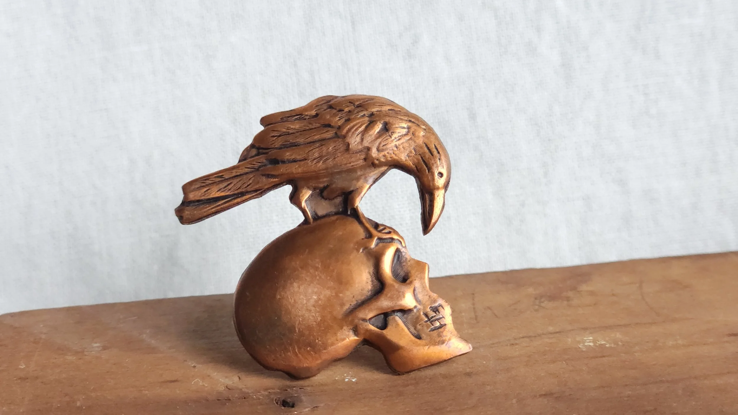 Die-struck hand sawn scatter pin depicting a raven atop a skull.