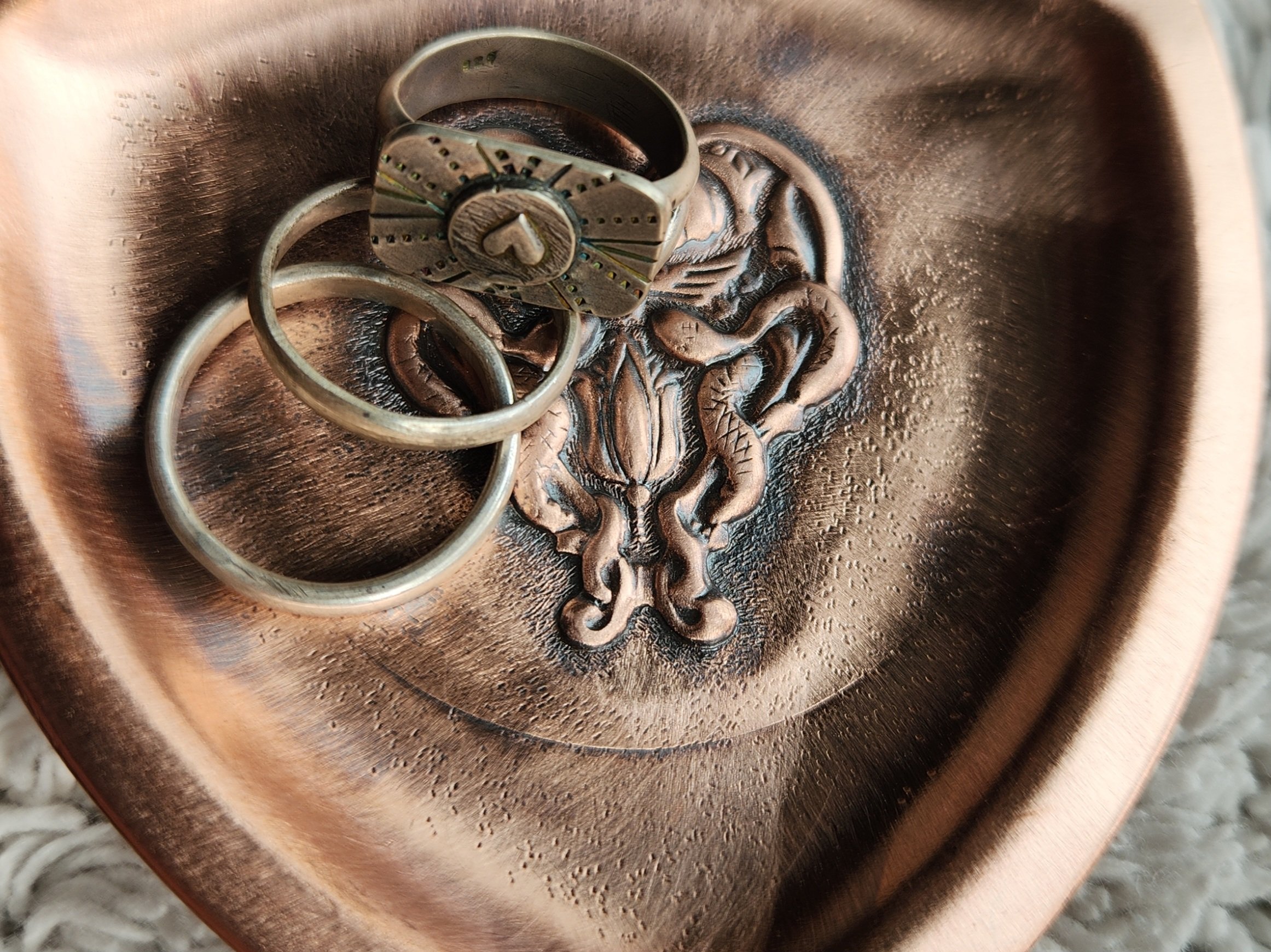 Hand formed and die-struck copper dish with Egyptian snake and scarab motif, holding three silver rings.