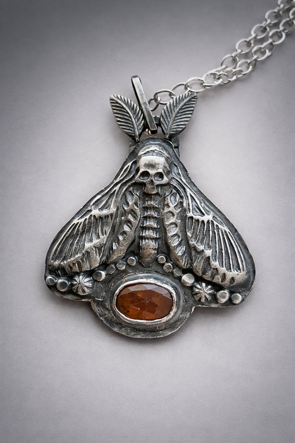 Die-struck and hand fabricated sterling silver moth necklace with orange kyanite accent.