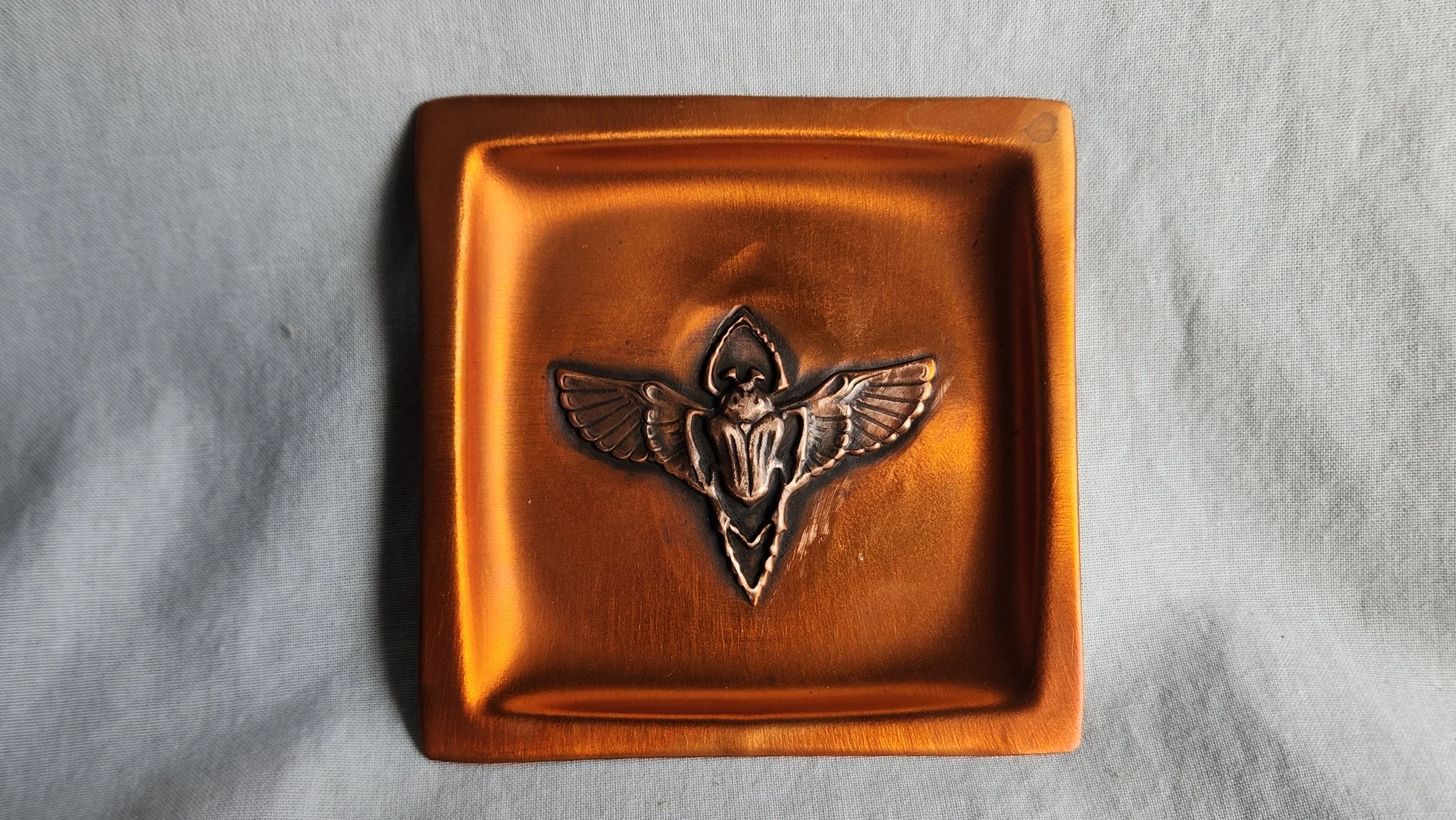 Die-struck and hand formed square copper dish featuring a scarab with outstretched legs and wings.