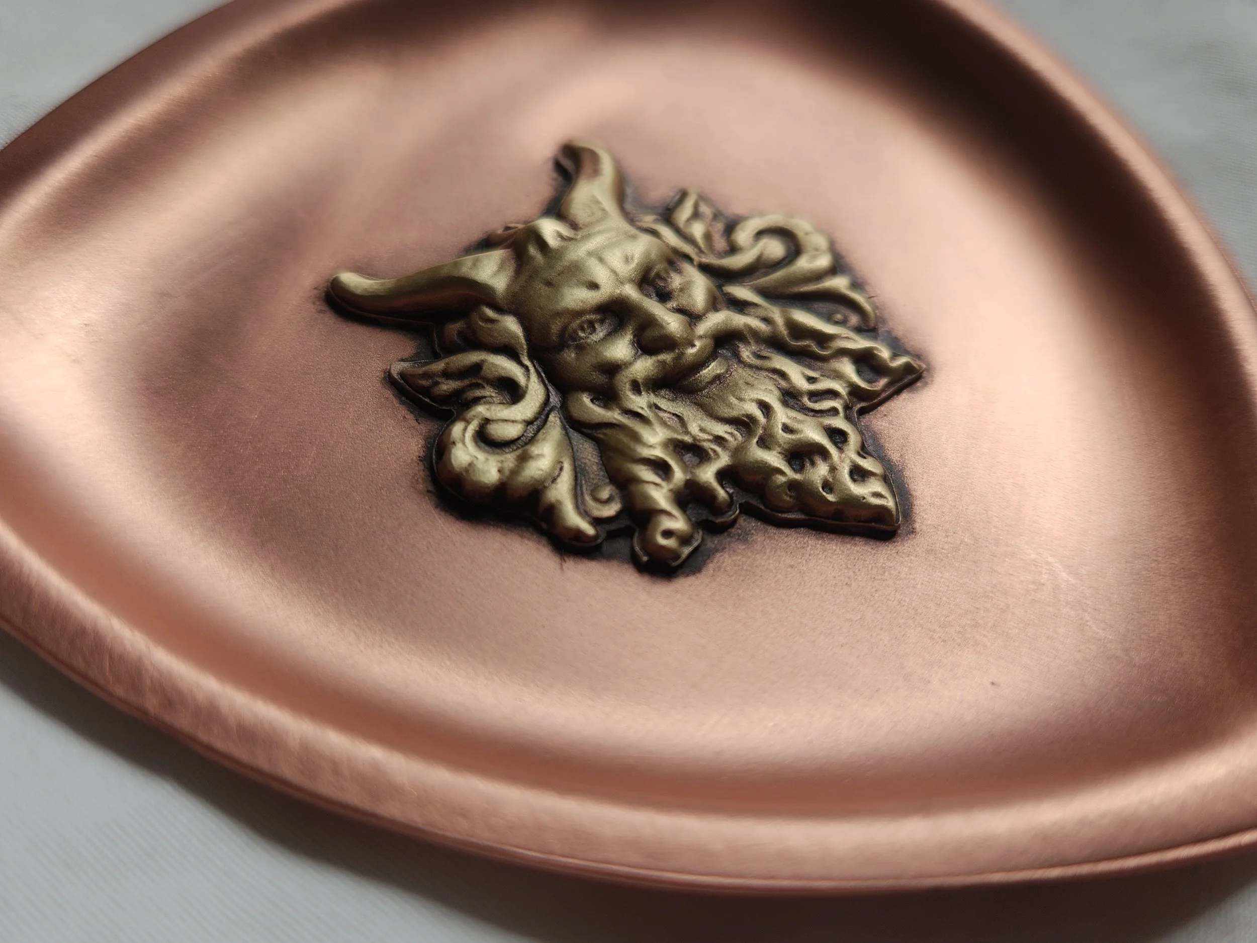 Trillion shaped copper dish with a die-struck brass depiction of a bearded satyr.