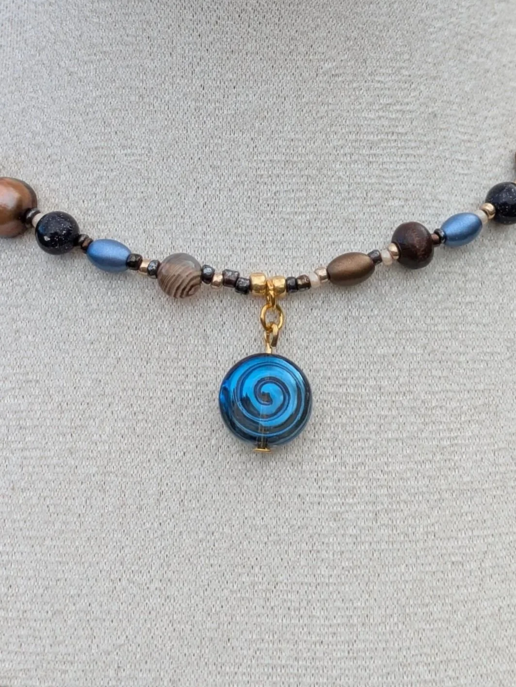 Necklace featuring beads of various colors and shapes, with a large blue spiral pendant centerpiece.