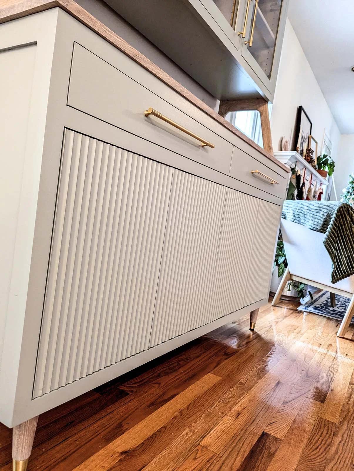 A beige modern sideboard with gold handles and tapered legs in a cozy living room decorated for Christmas.
