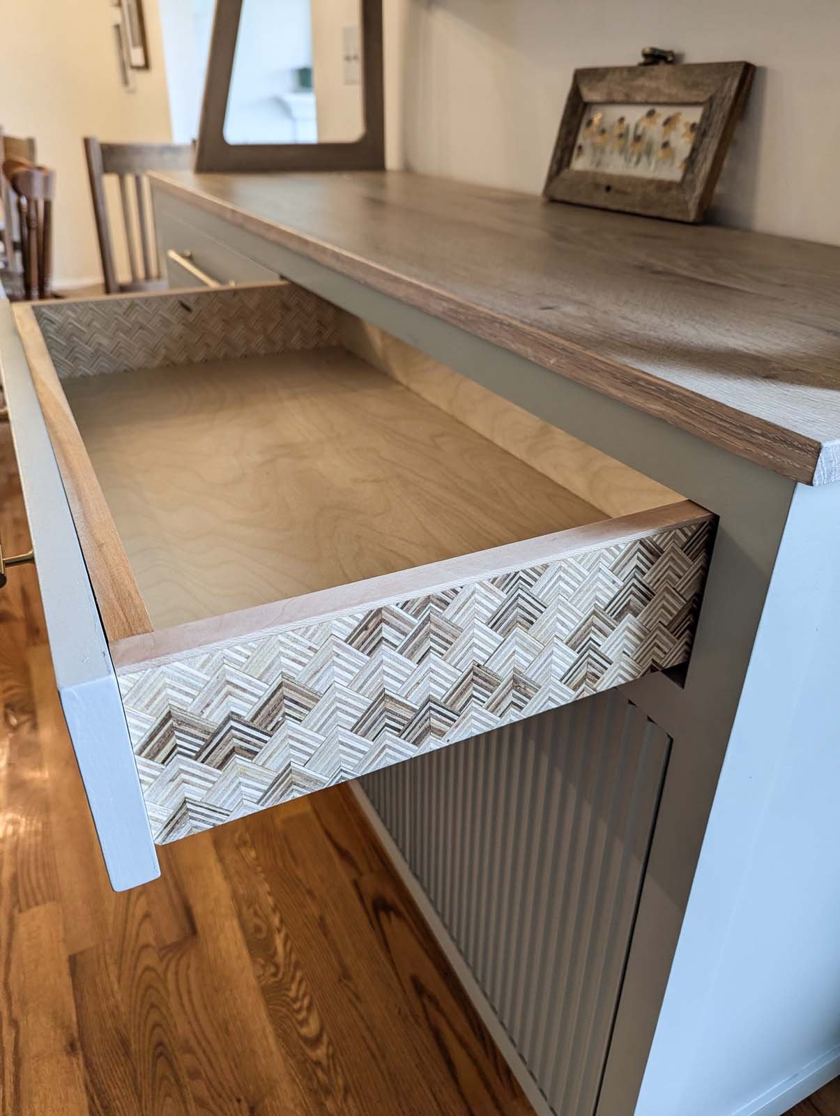 Coffee table with a geometric patterned drawer and a wooden top, located in a living room with wooden flooring and decorative pictures on the wall.