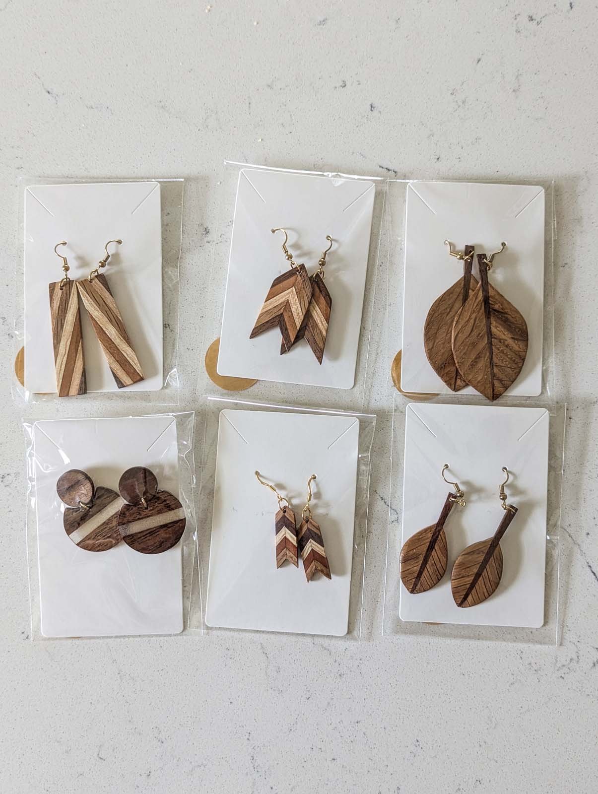 Set of six pairs of wooden and patterned earrings on individual white display cards, arranged in two rows on a light surface.