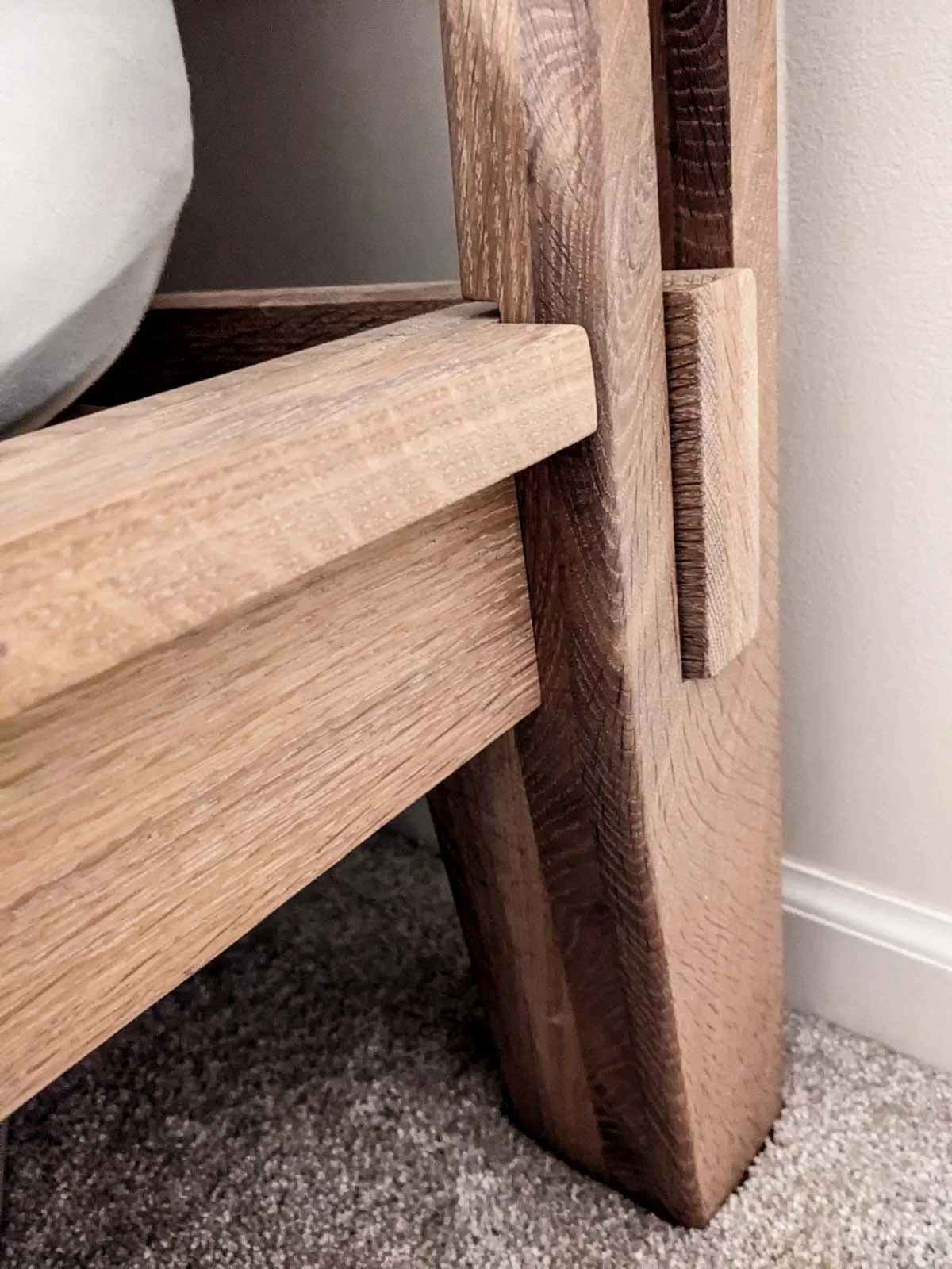 Close-up of a wooden furniture piece with light and dark wood, showing the corner joint with visible grain and texture.