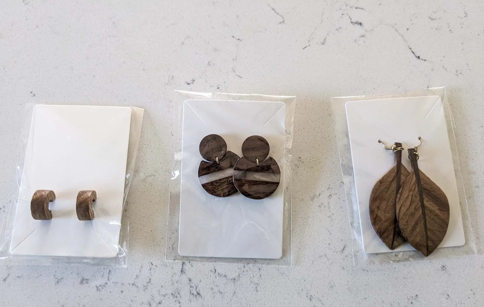 Three pairs of wooden earrings on white display cards, arranged from left to right.