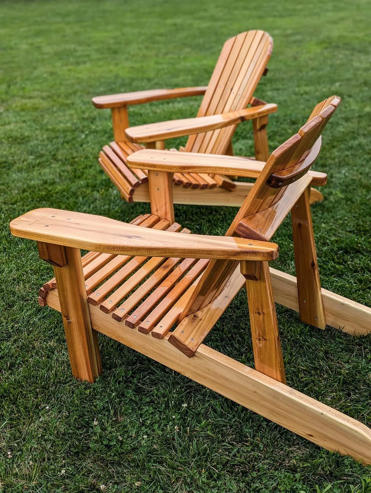 Two wooden Adirondack chairs on a grassy lawn.