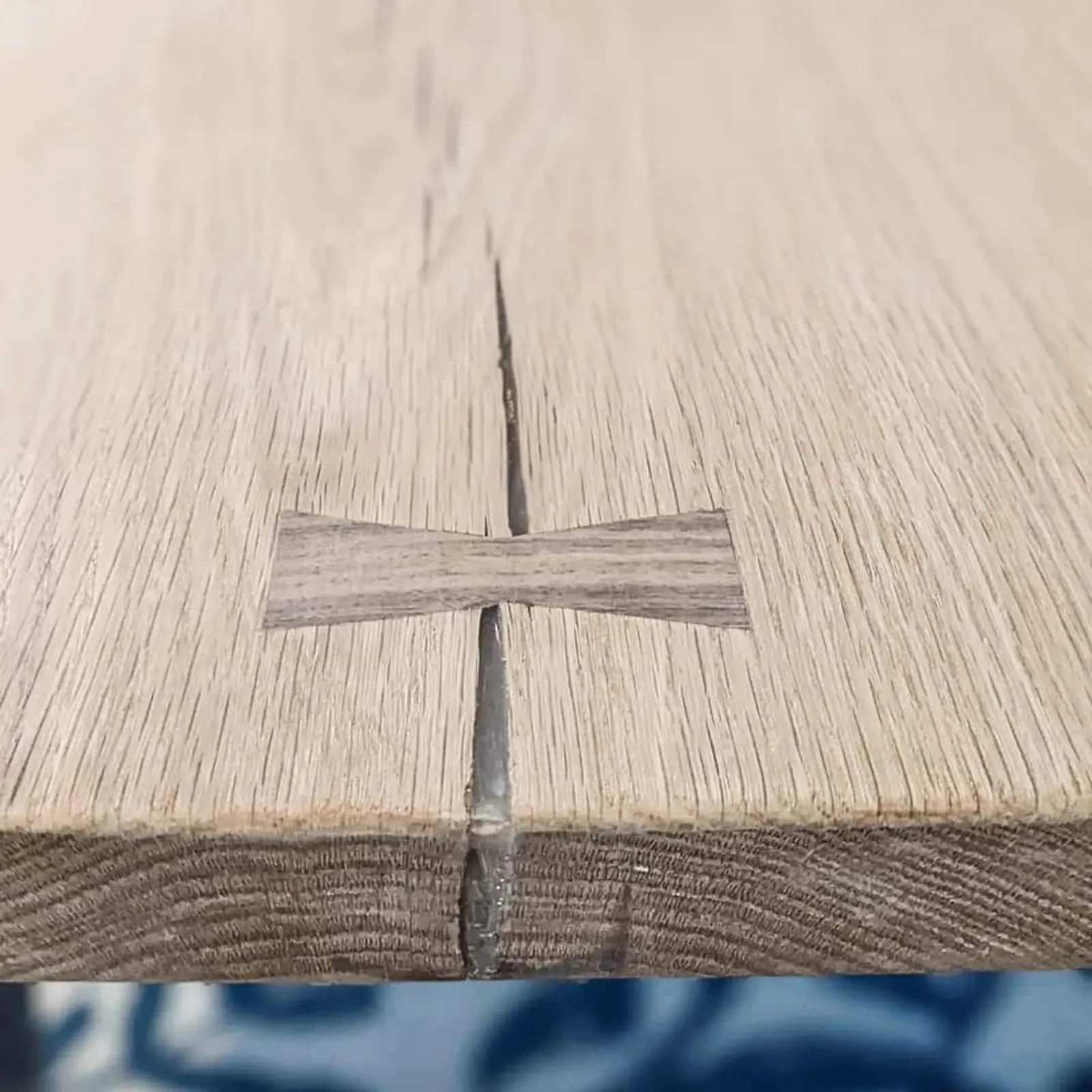 Close-up of a wooden surface with a small cross-shaped inlay in the center, and a visible crack running along the length of the wood.