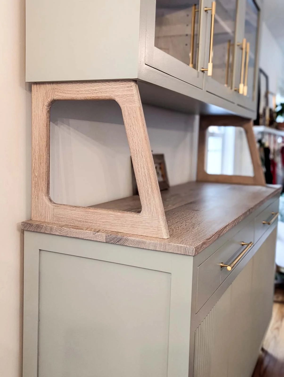 Close-up of a light-green cabinet with a wooden countertop and decorative gold handles, with a wooden picture frame leaning against the wall.