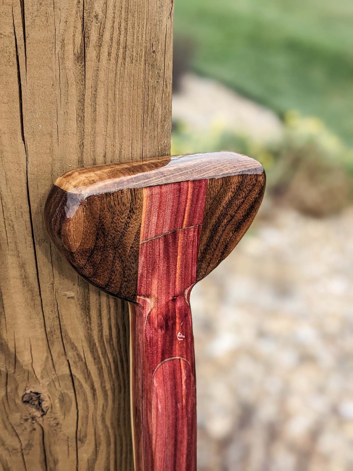 Close-up of a wooden mallet with a padded head, attached to a wooden post, outdoors.