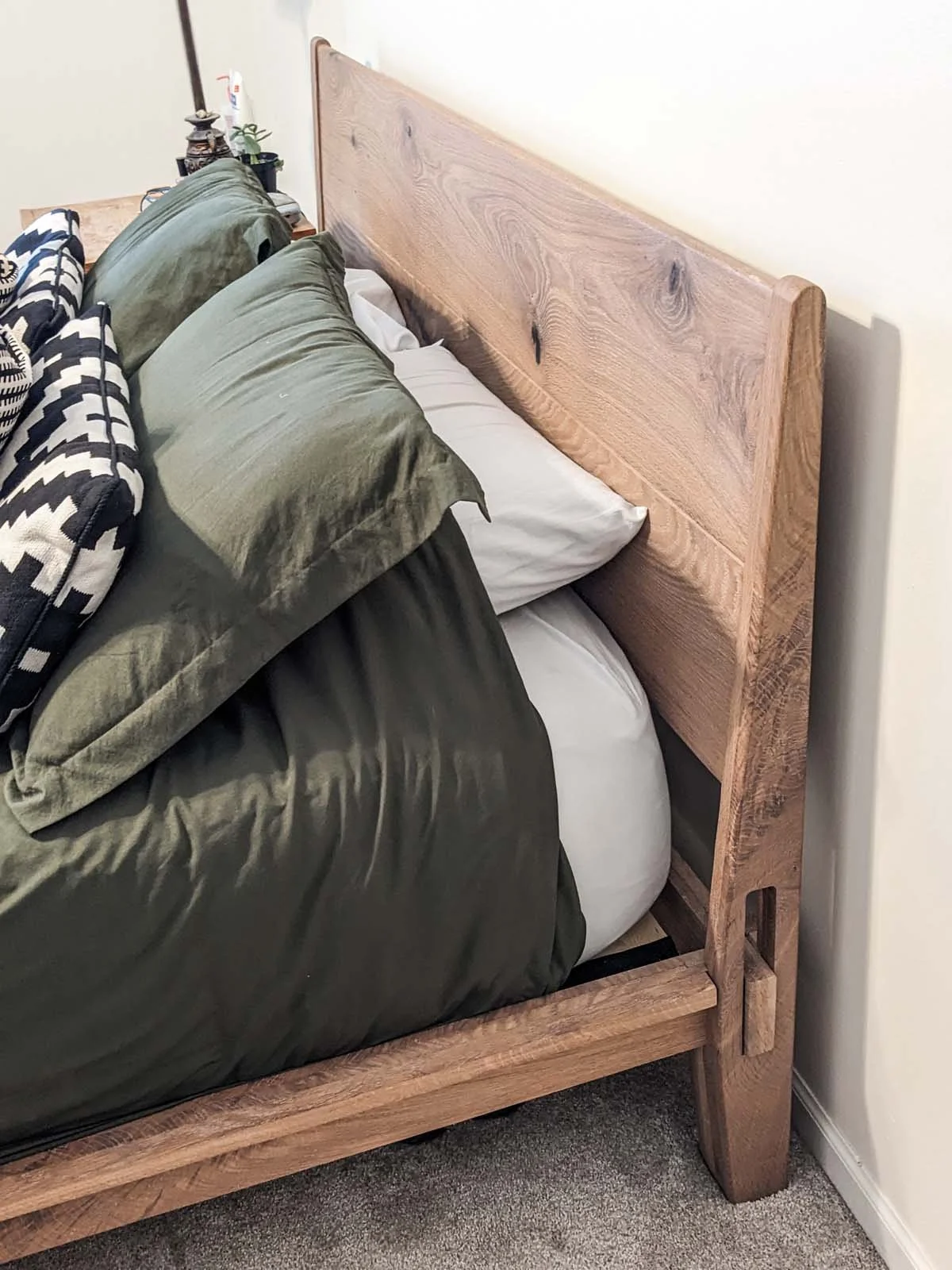Close-up of a wooden bed with a rustic headboard, unmade bedding, and pillows on a carpeted floor.
