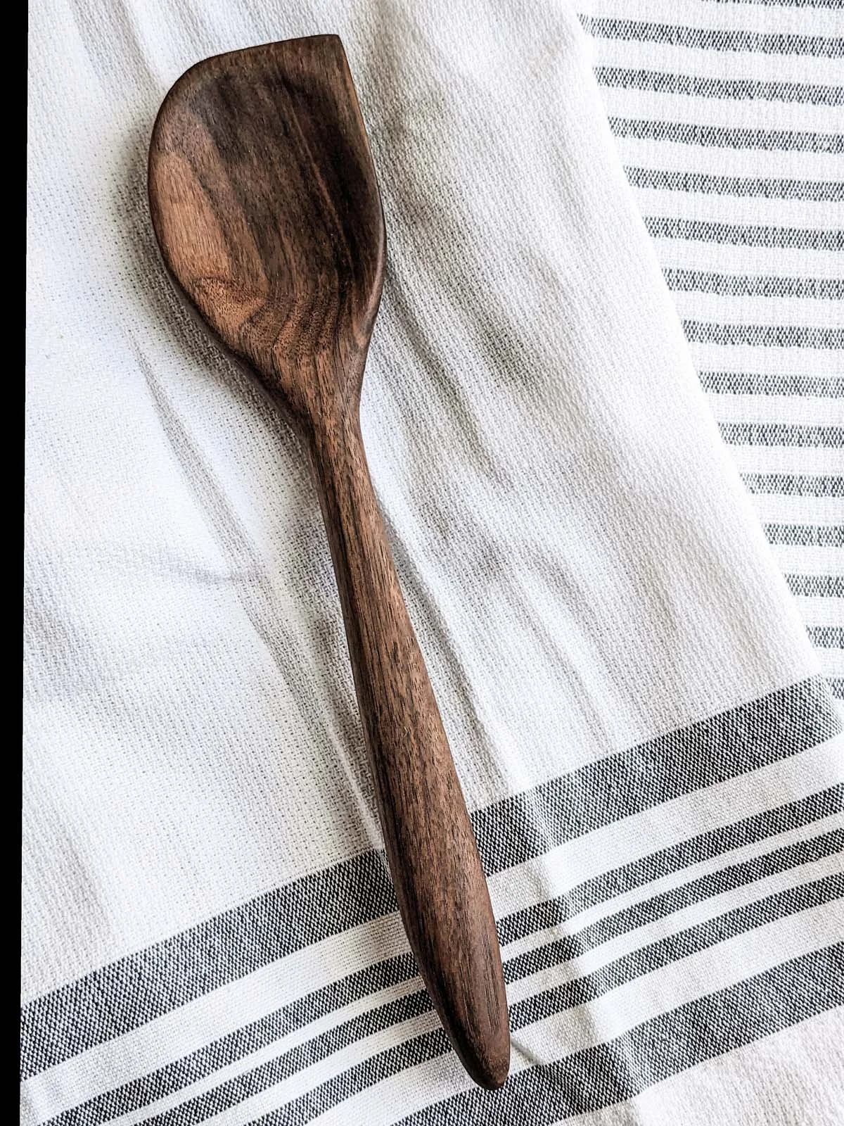 A wooden spatula resting on a white cloth with black and gray stripes.