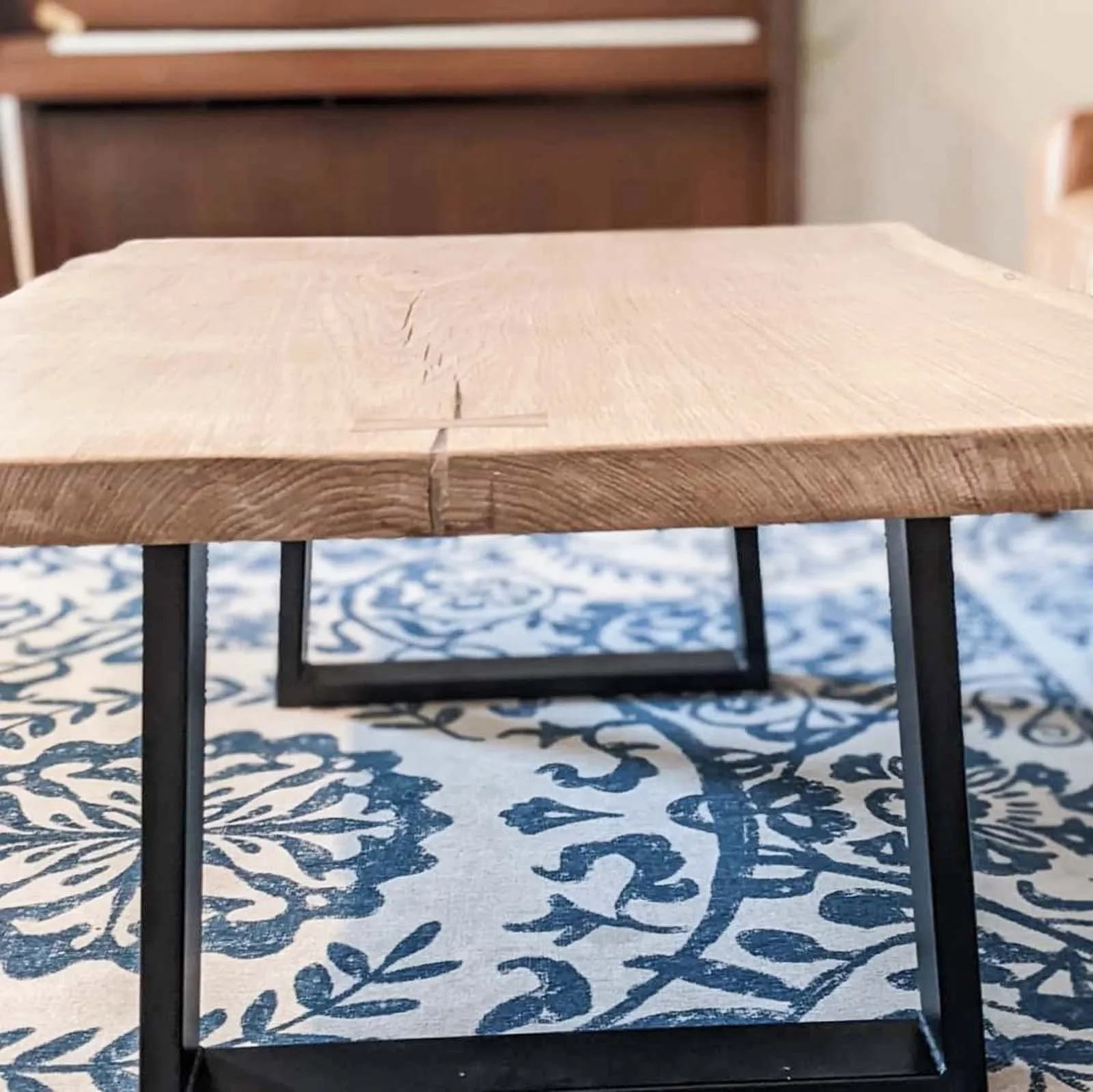 Close-up of a wooden and metal table with a patterned blue and white tablecloth underneath.